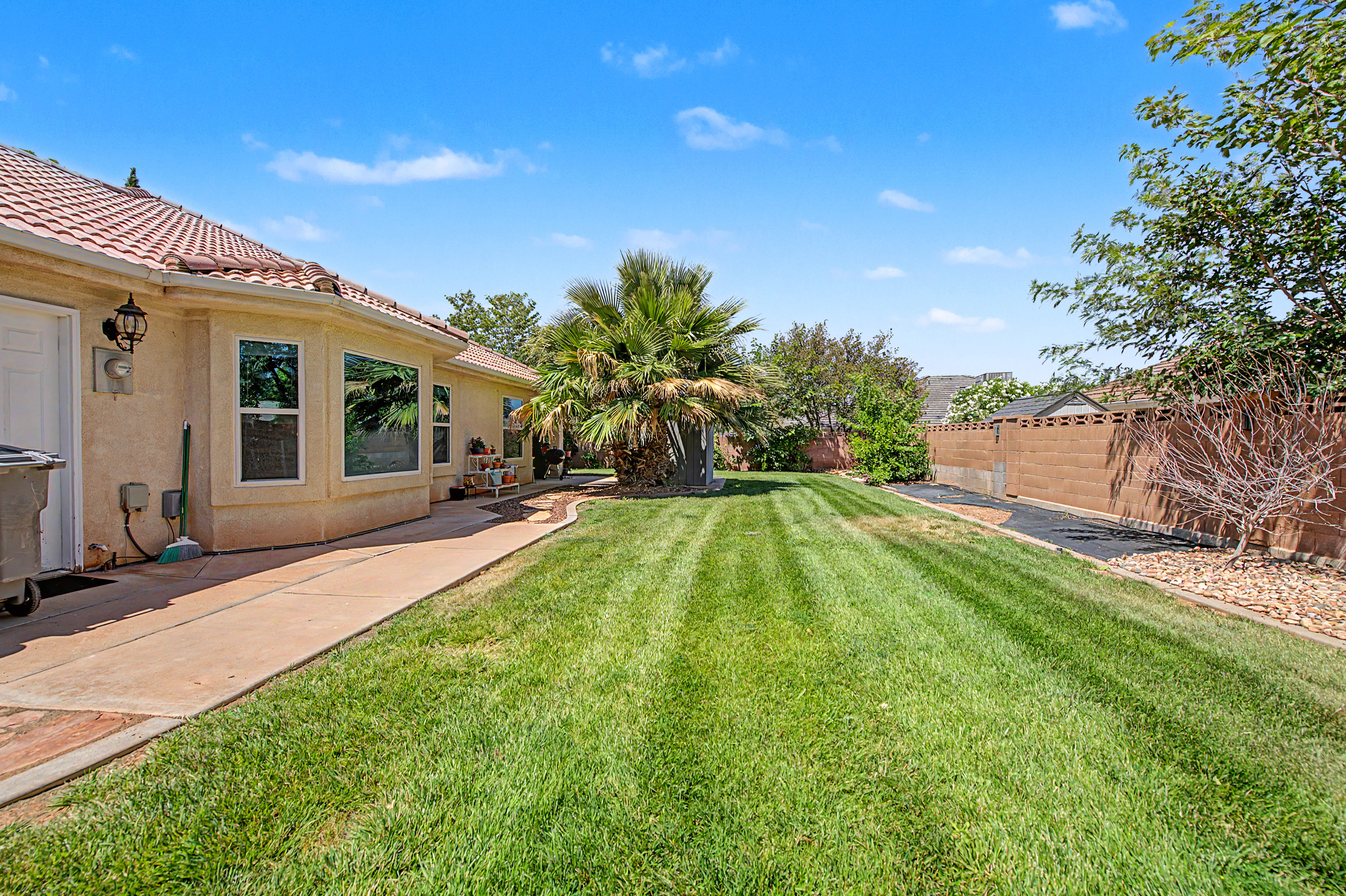 Spacious rear yard featuring an expansive lawn, concrete patio, mature landscaping, and a privacy wall