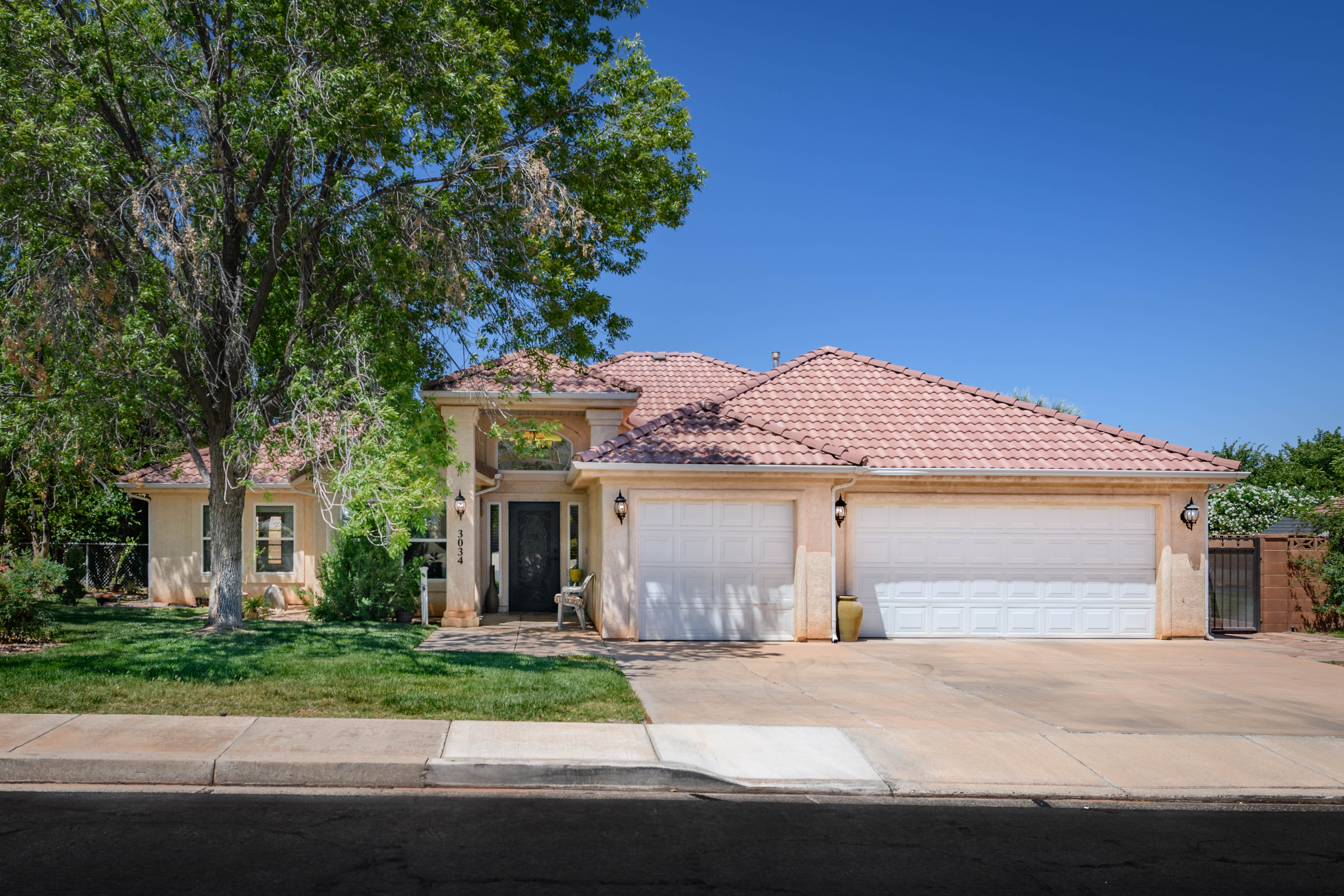 Stucco exterior home featuring a covered entry, two garage doors, concrete driveway, and mature landscaping