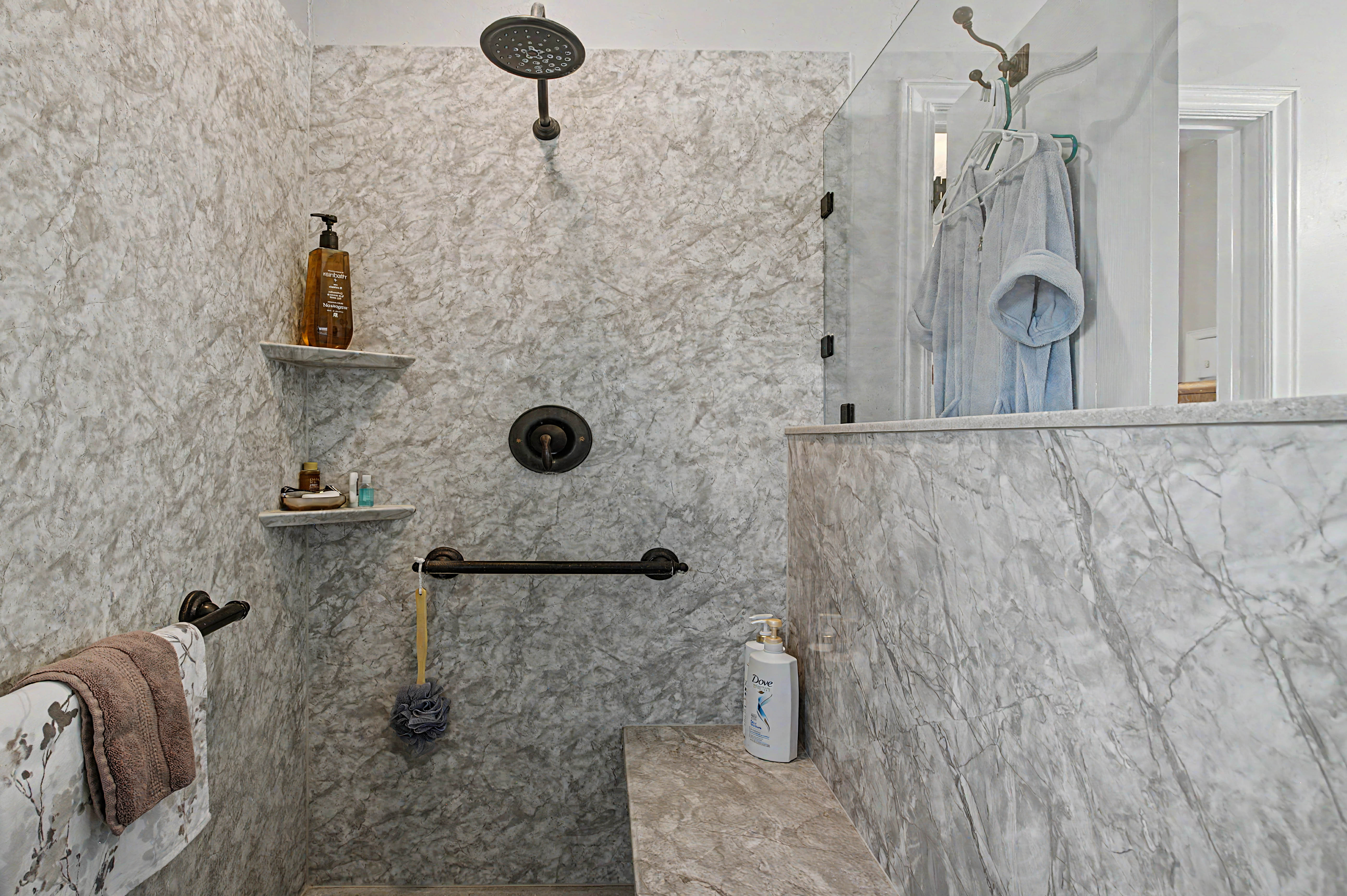 Walk-in shower with full-height stone-finish wall panels, a built-in bench, and a rain showerhead