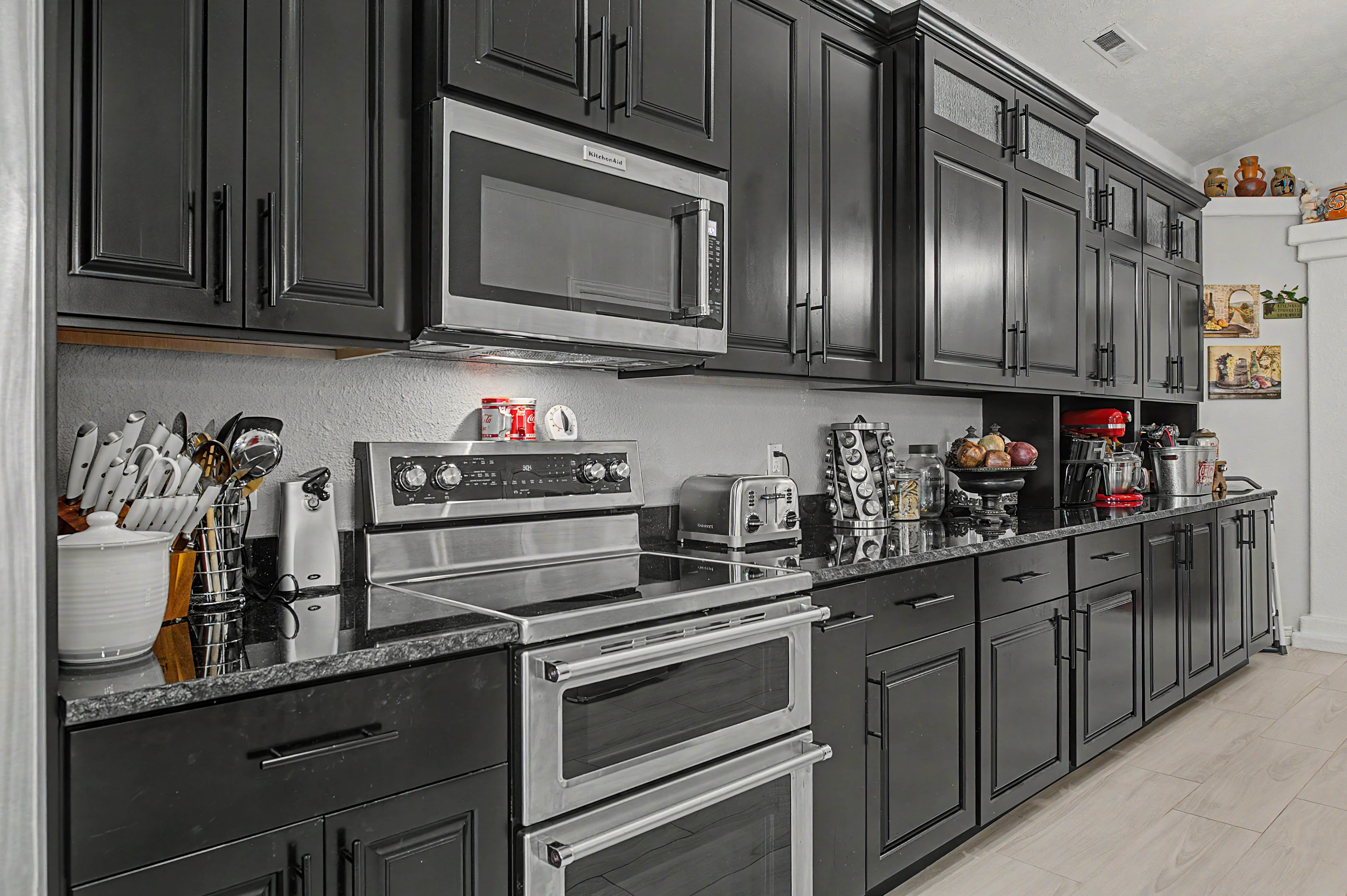 Kitchen featuring abundant dark-finish cabinetry, stainless steel appliances, a built-in microwave, and stone countertops