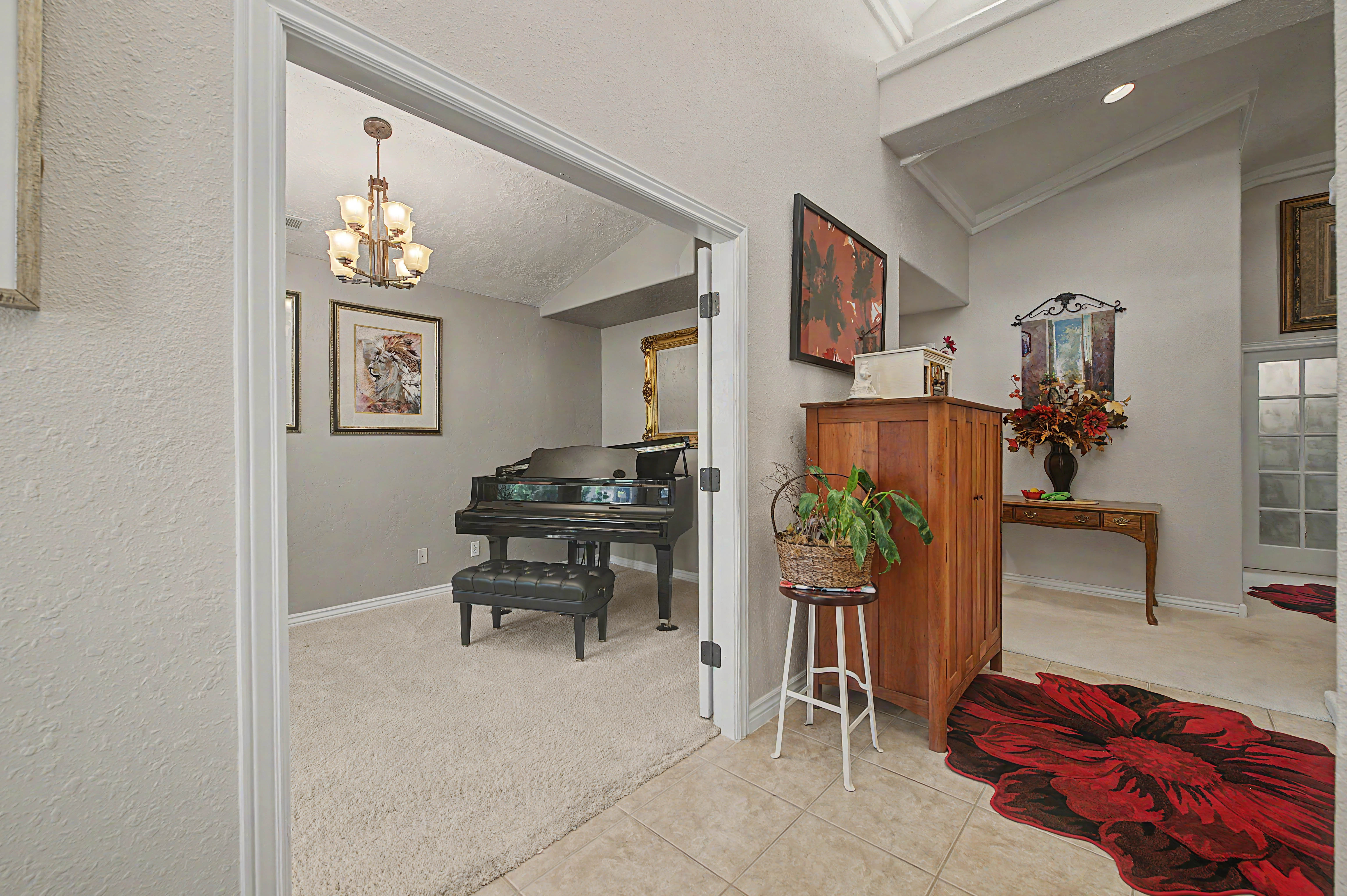 Entryway featuring a vaulted ceiling and tile flooring, opening to a carpeted room with a multi-arm chandelier