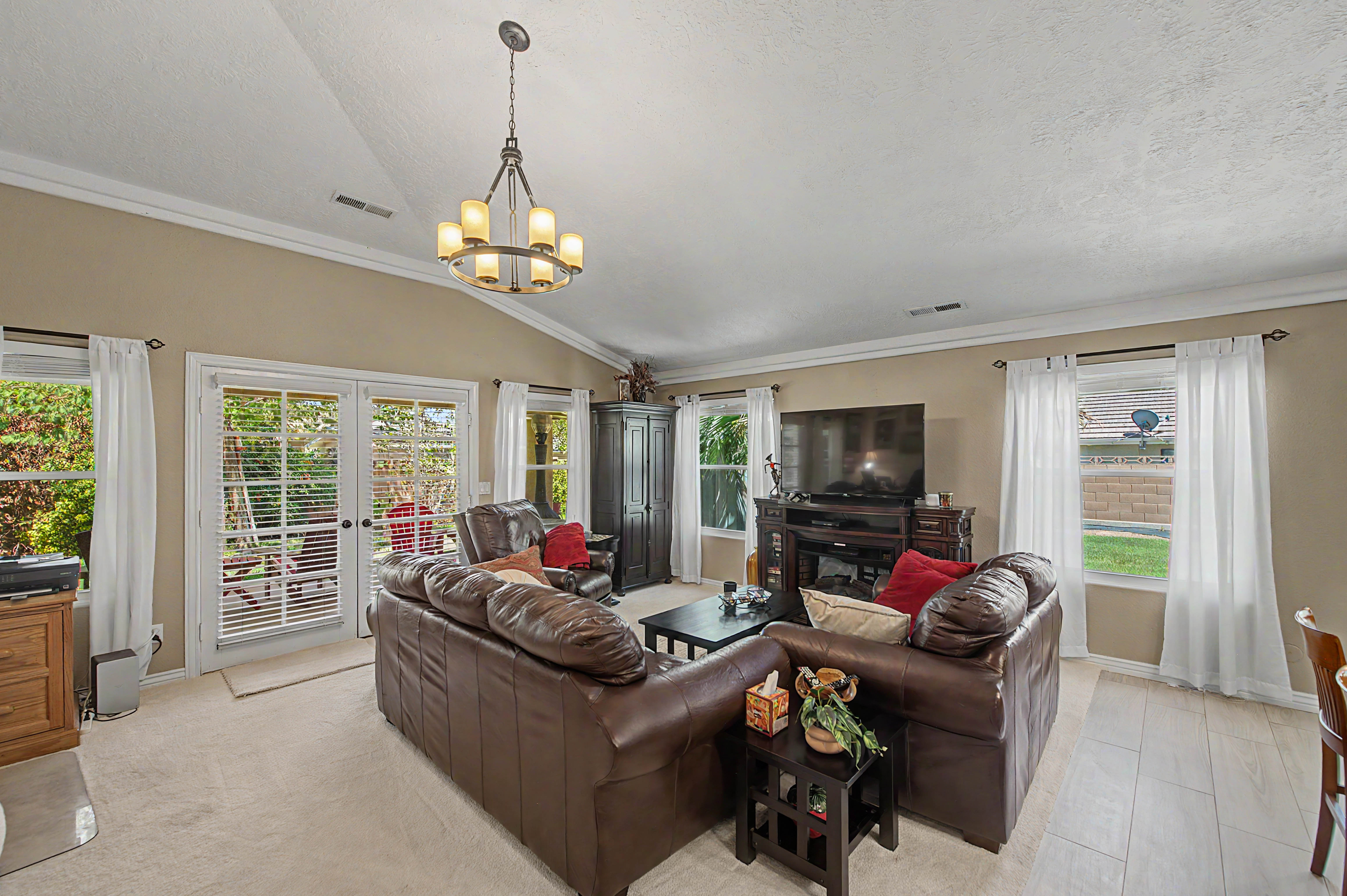Living area featuring vaulted ceilings, a central chandelier, multiple windows, double glass doors, and a combination of carpet and wood-finish flooring