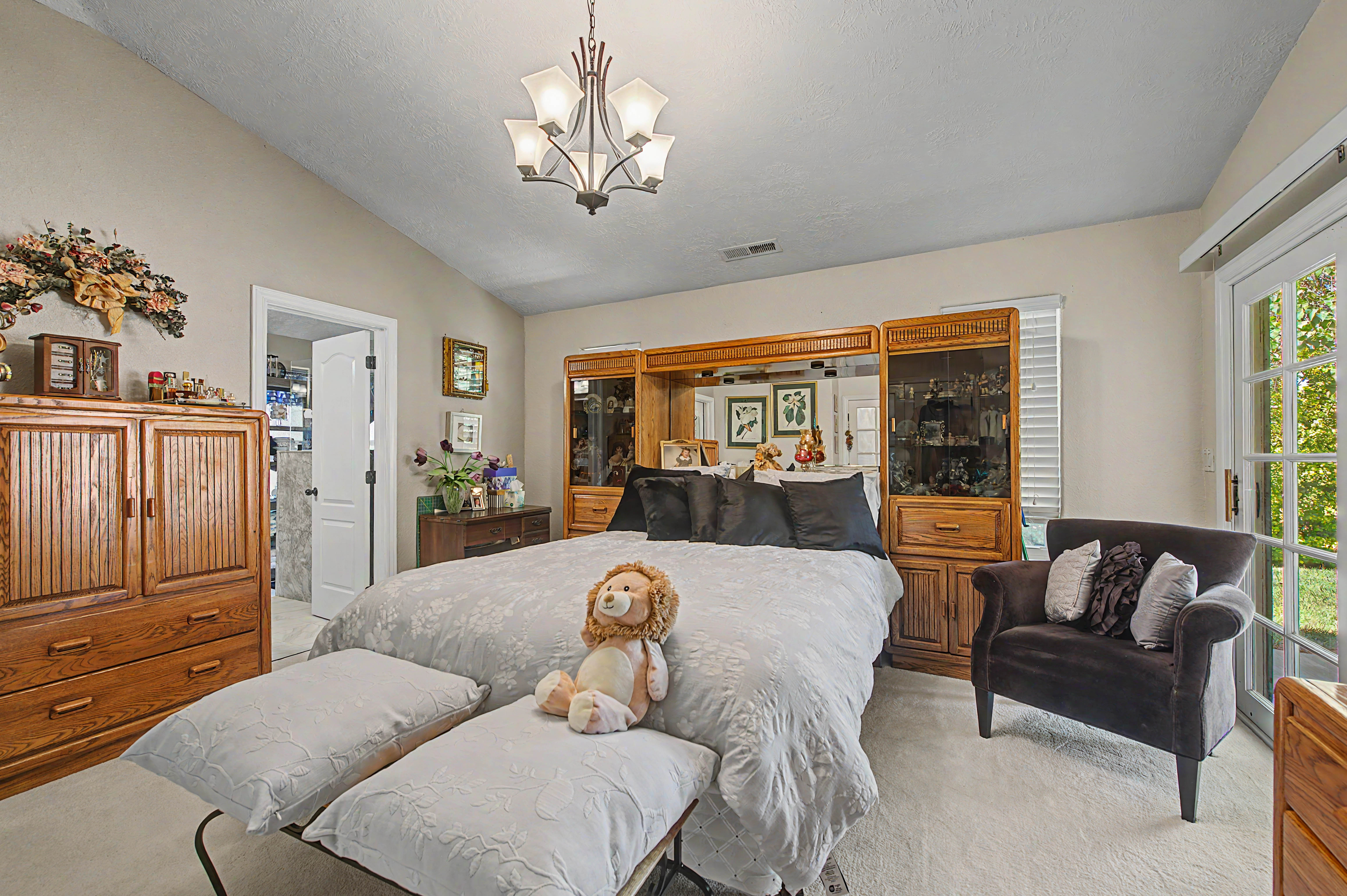 Spacious room featuring vaulted ceilings, a multi-light chandelier, a built-in wall unit with mirrored backing and display cabinetry, and double French doors with interior blinds