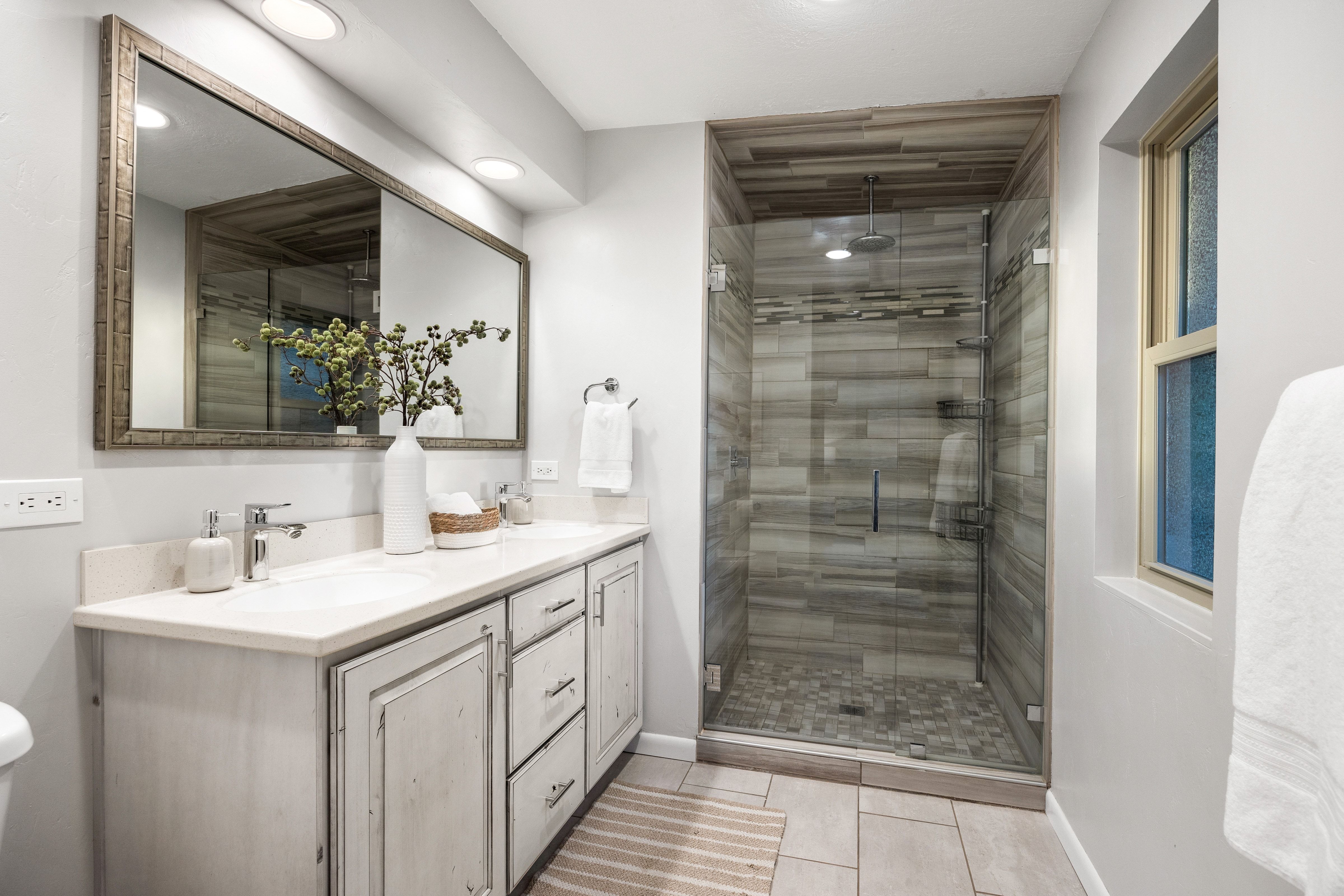 Glass-enclosed shower featuring a rain shower head, horizontal tile work, and pebble-style floor