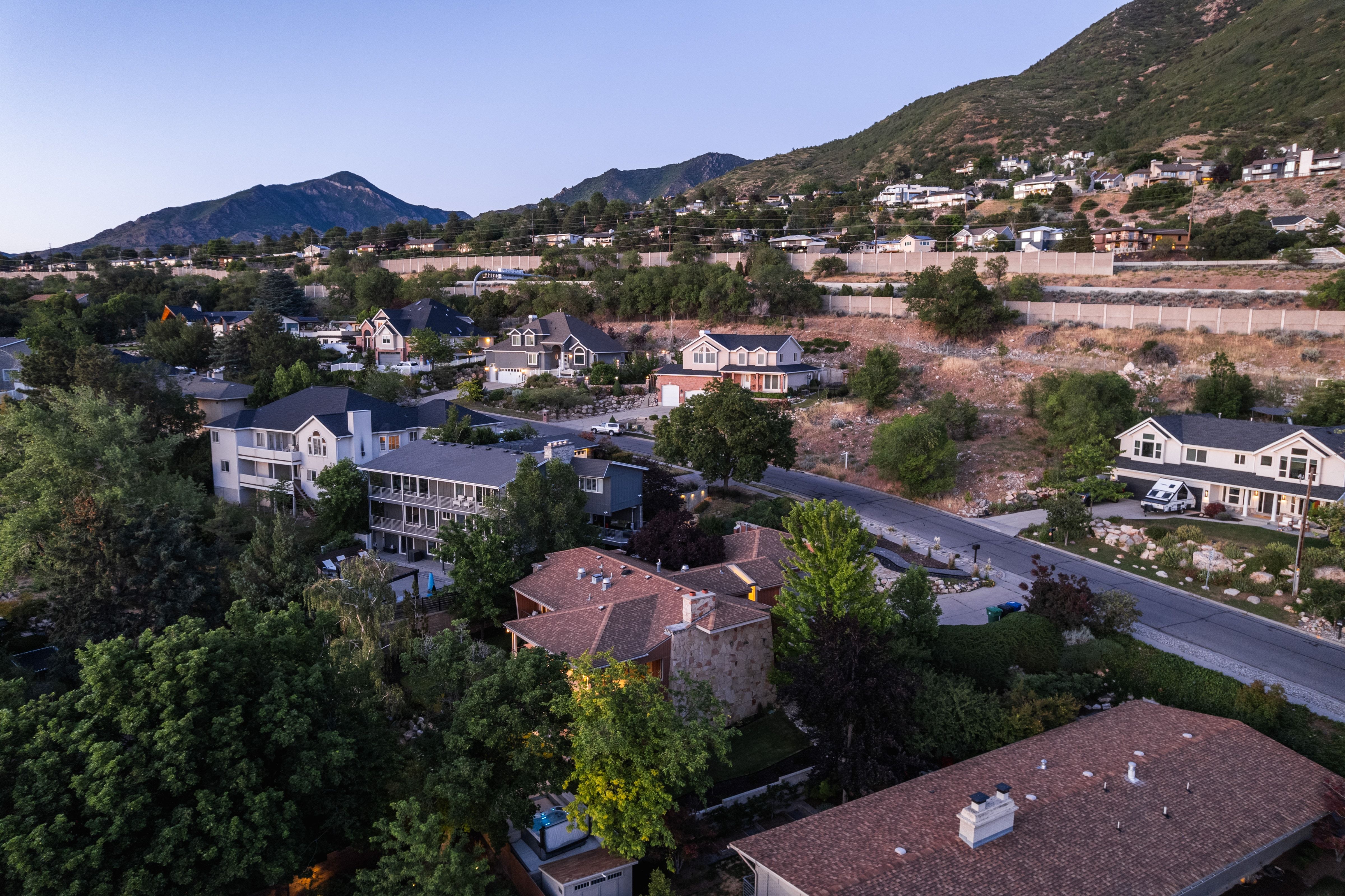 Sloping terrain with established homes featuring diverse architectural styles, mature trees, and mountainous backdrops