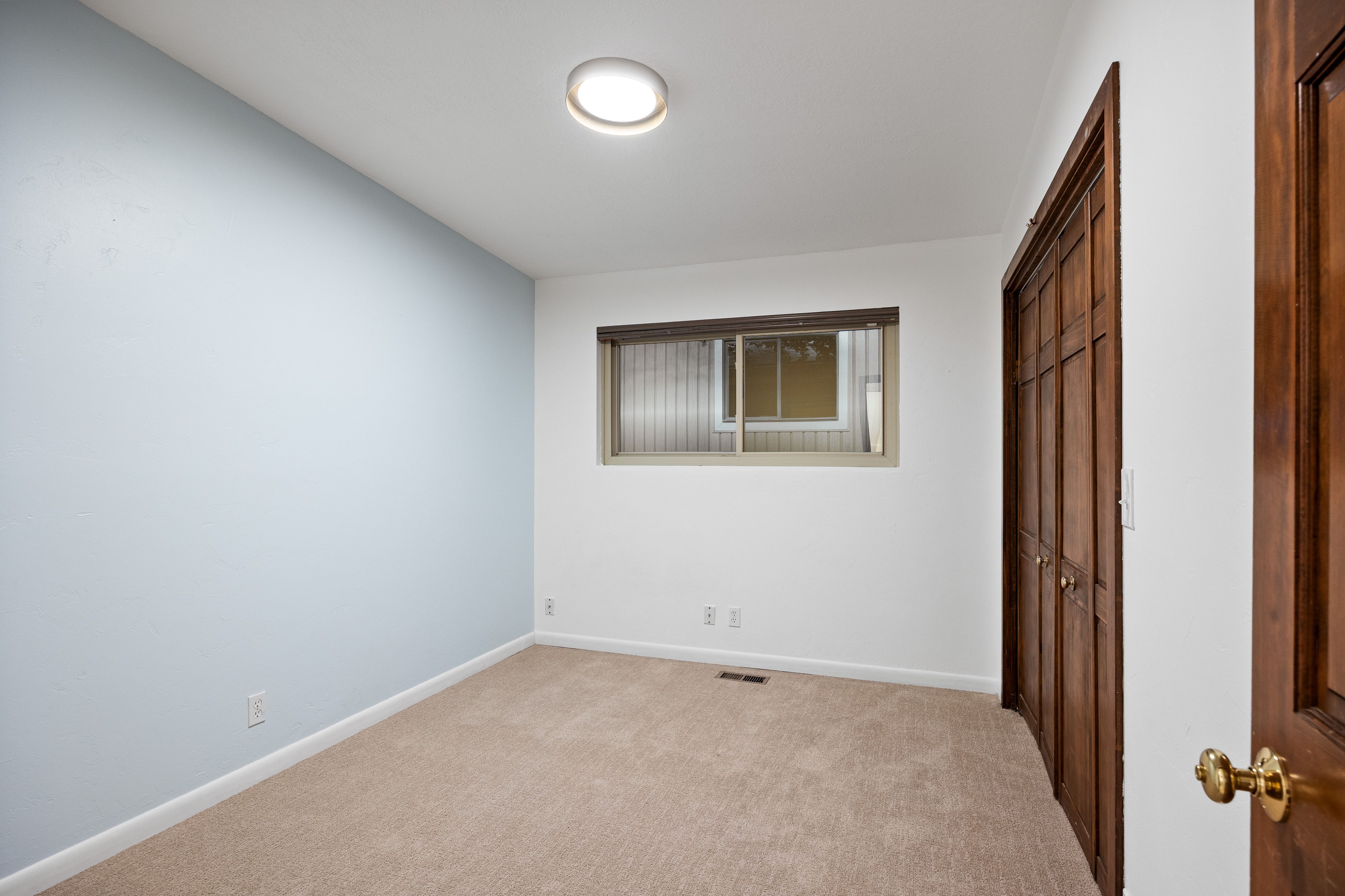Room featuring a neutral carpet, a light blue accent wall, white painted walls, a window with a wood frame, and a flush-mount ceiling light fixture
