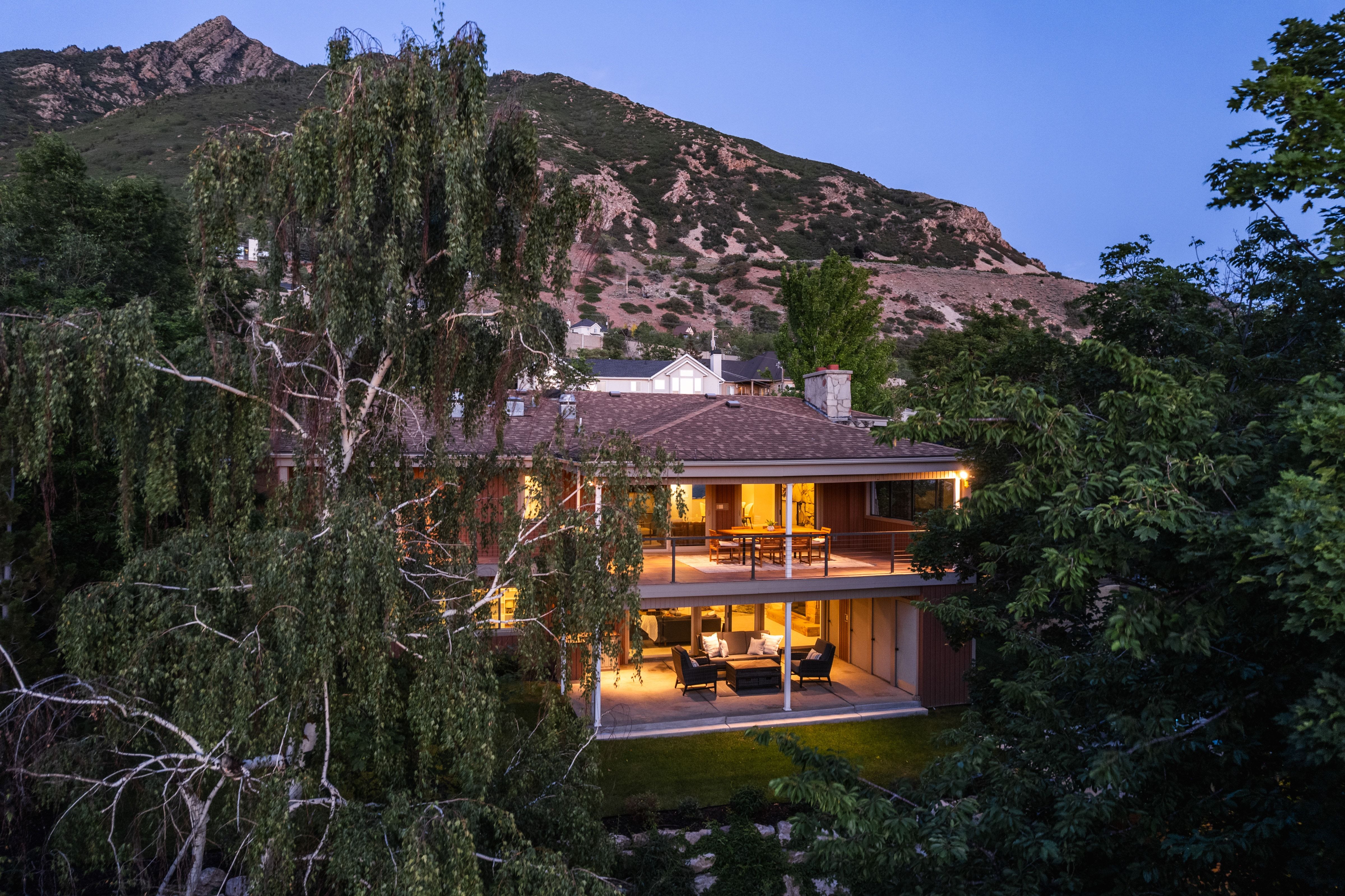 Terraced property featuring two covered patios with metal railings, a visible brown shingle roof, and a prominent mountain backdrop