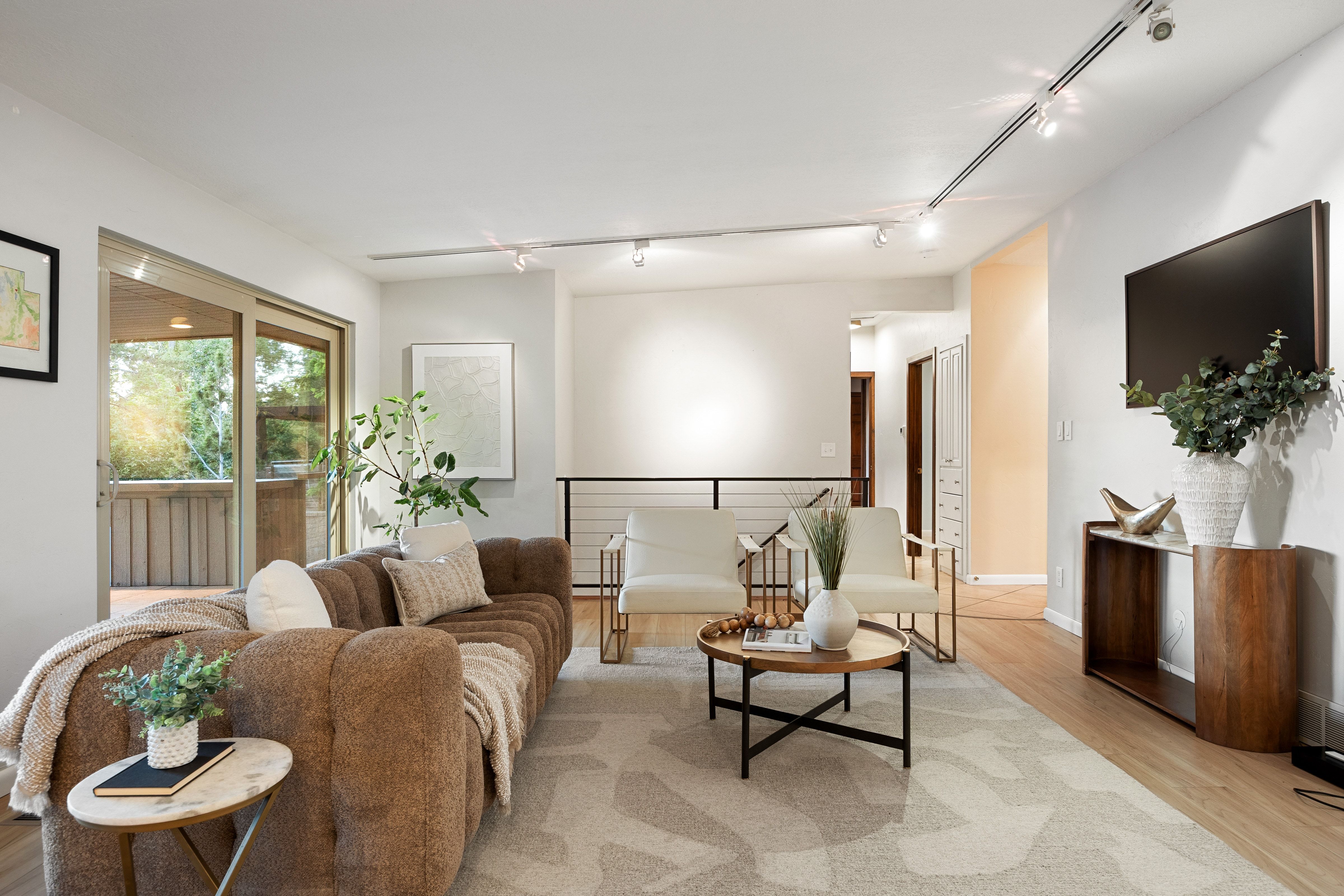 Bright living area featuring wood-finish flooring, sliding glass doors to an outdoor deck, a black metal railing, and recessed track lighting
