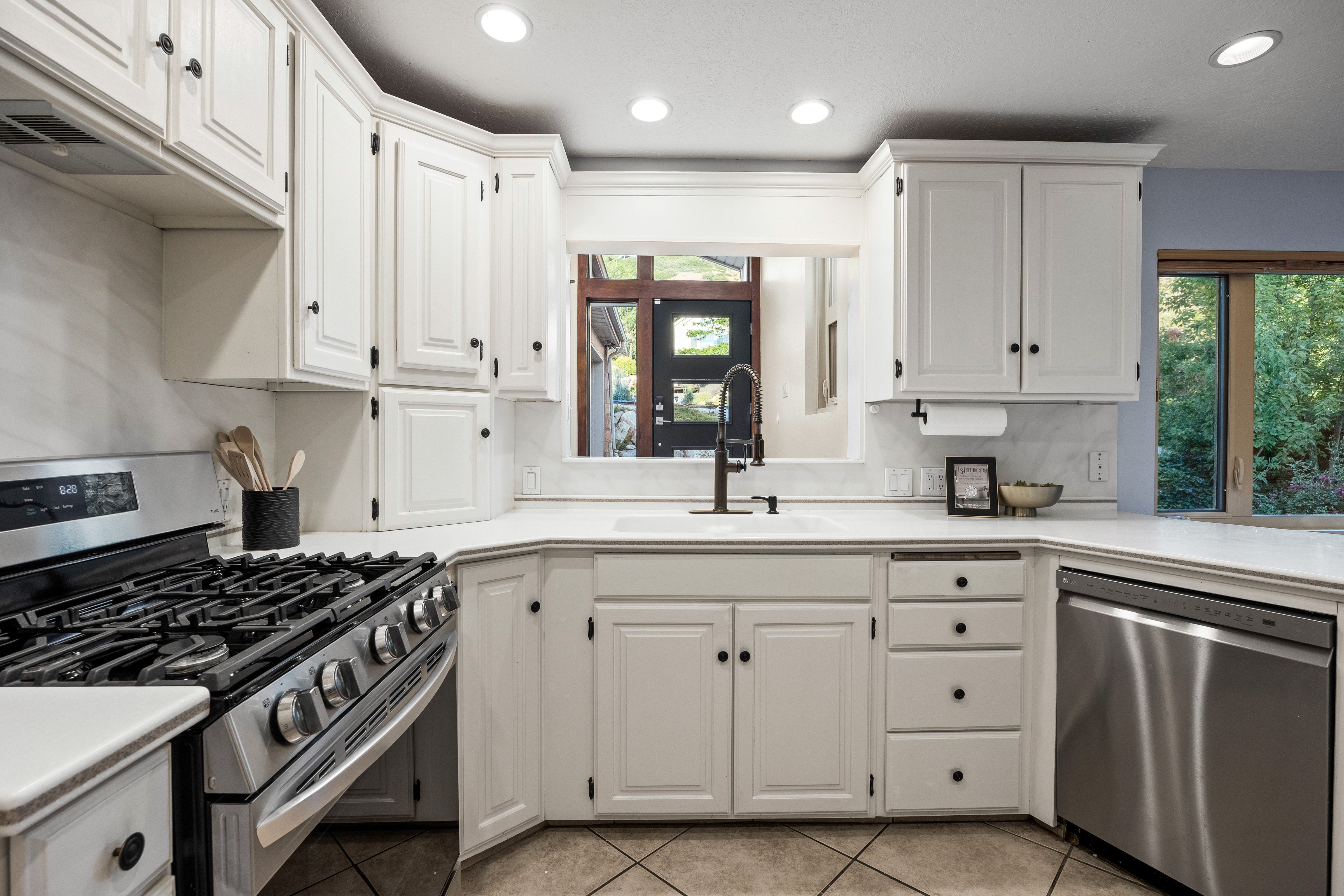 Kitchen featuring white shaker-style cabinetry, a built-in stainless steel gas range, a stainless steel dishwasher, white countertops, and a white tile backsplash