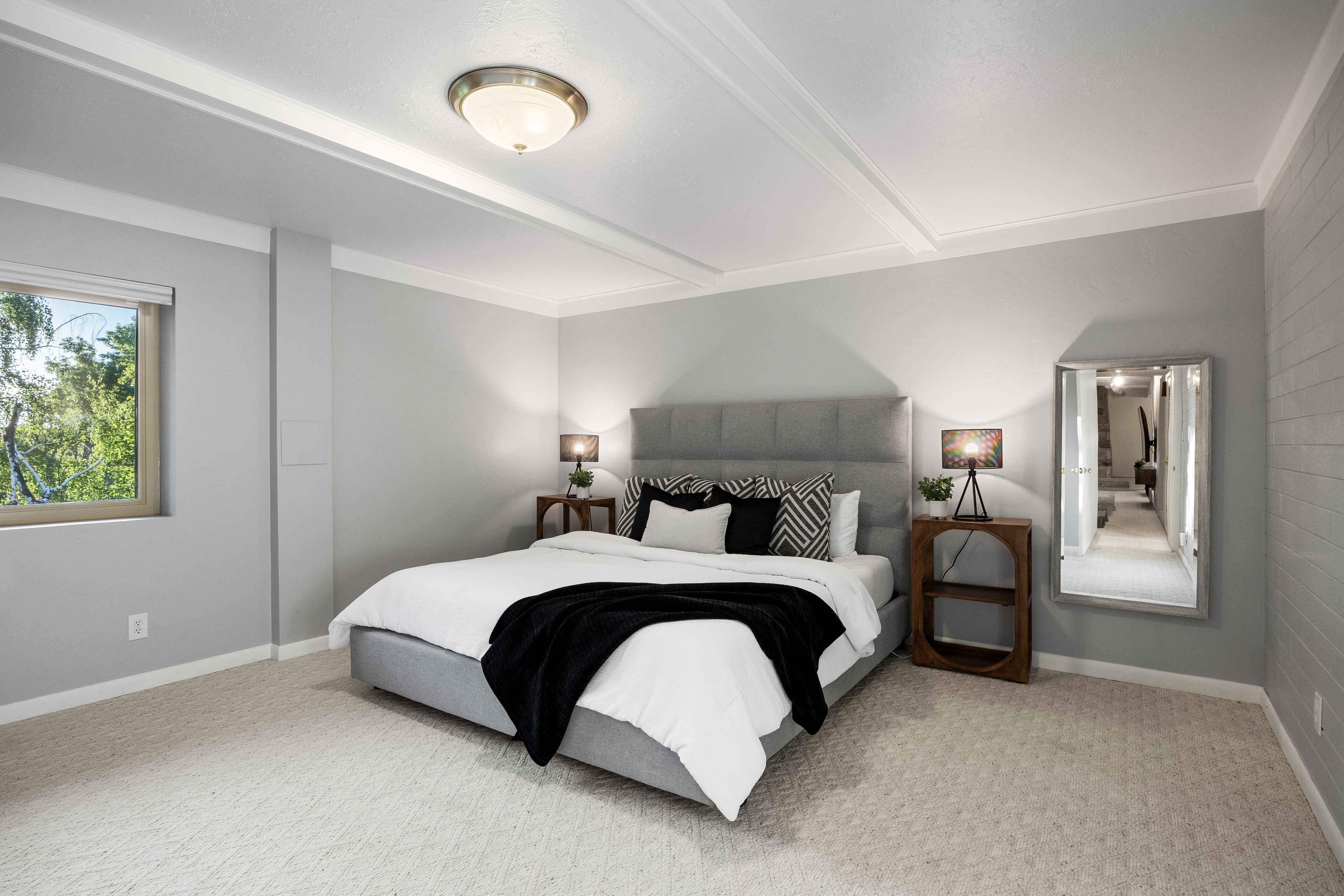 Bedroom featuring textured light gray walls, an upholstered headboard, a window with a roller shade, and an overhead flush-mount light fixture