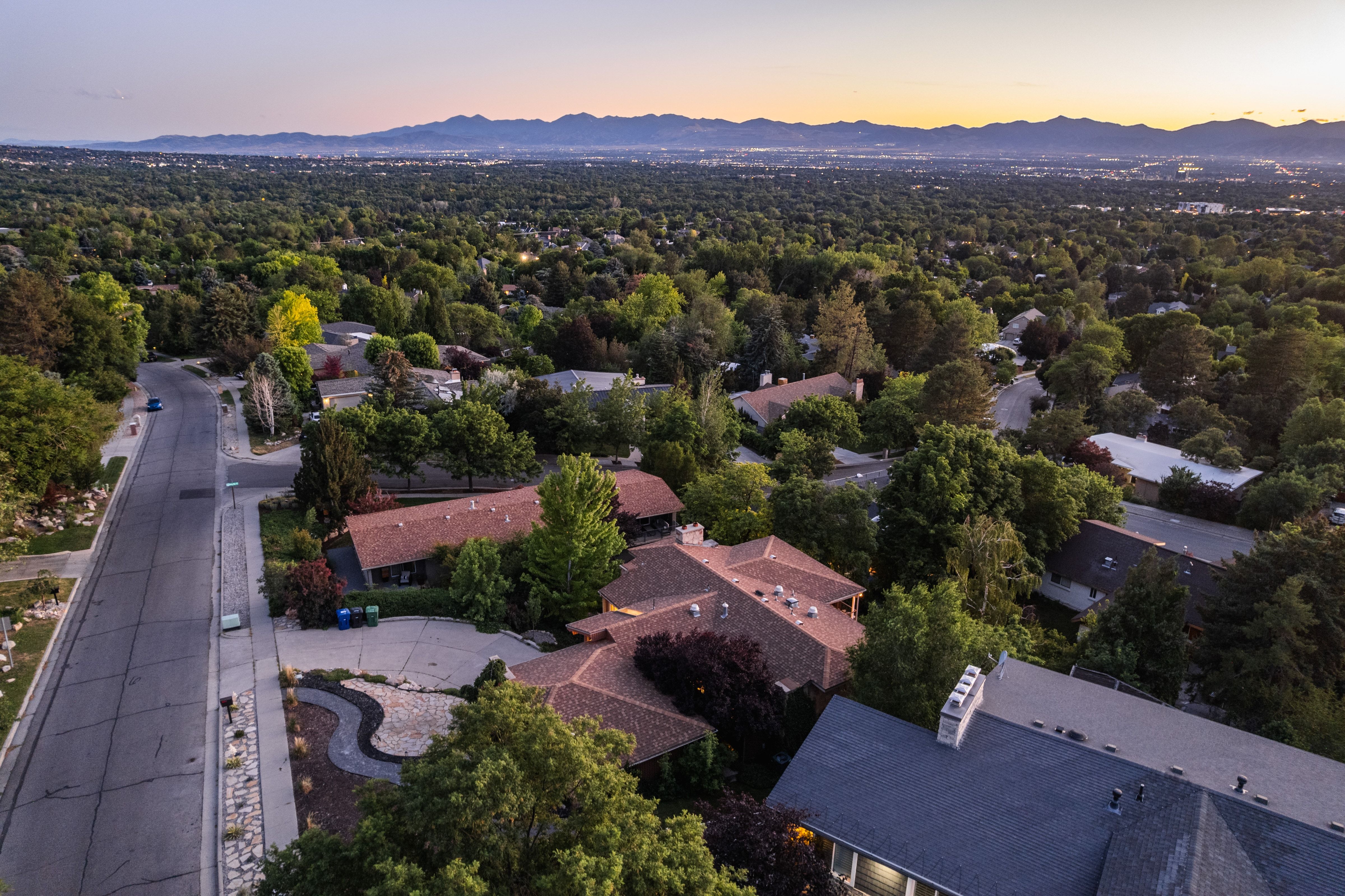 Residential area featuring numerous mature trees, paved streets, and mountain backdrop