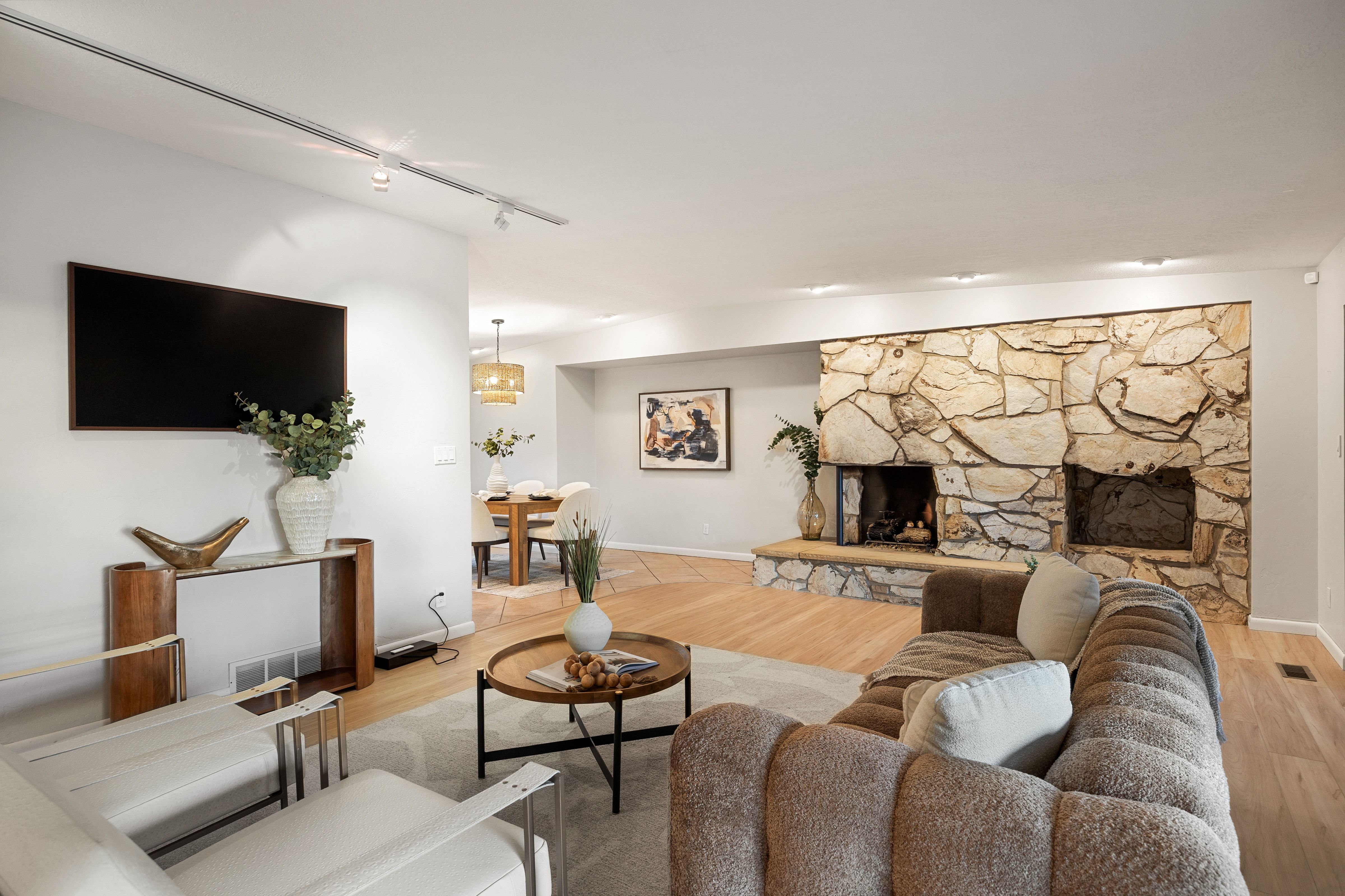 Living room featuring a large stone fireplace, light wood-finish flooring, recessed lighting, track lighting, and a neutral color palette