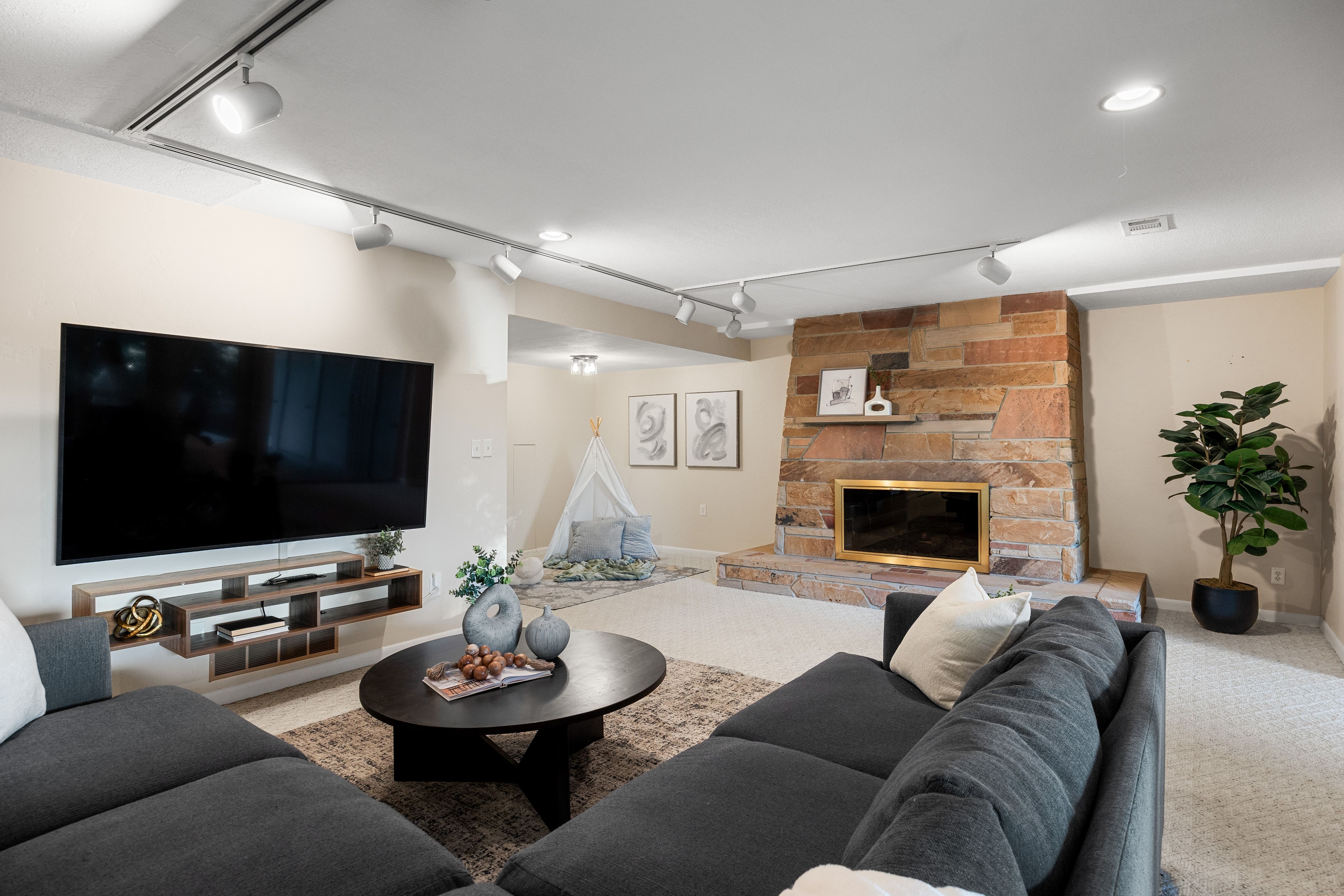 Living space featuring a stone fireplace with a brass-trimmed firebox, track lighting, recessed lighting, and light-toned carpeting