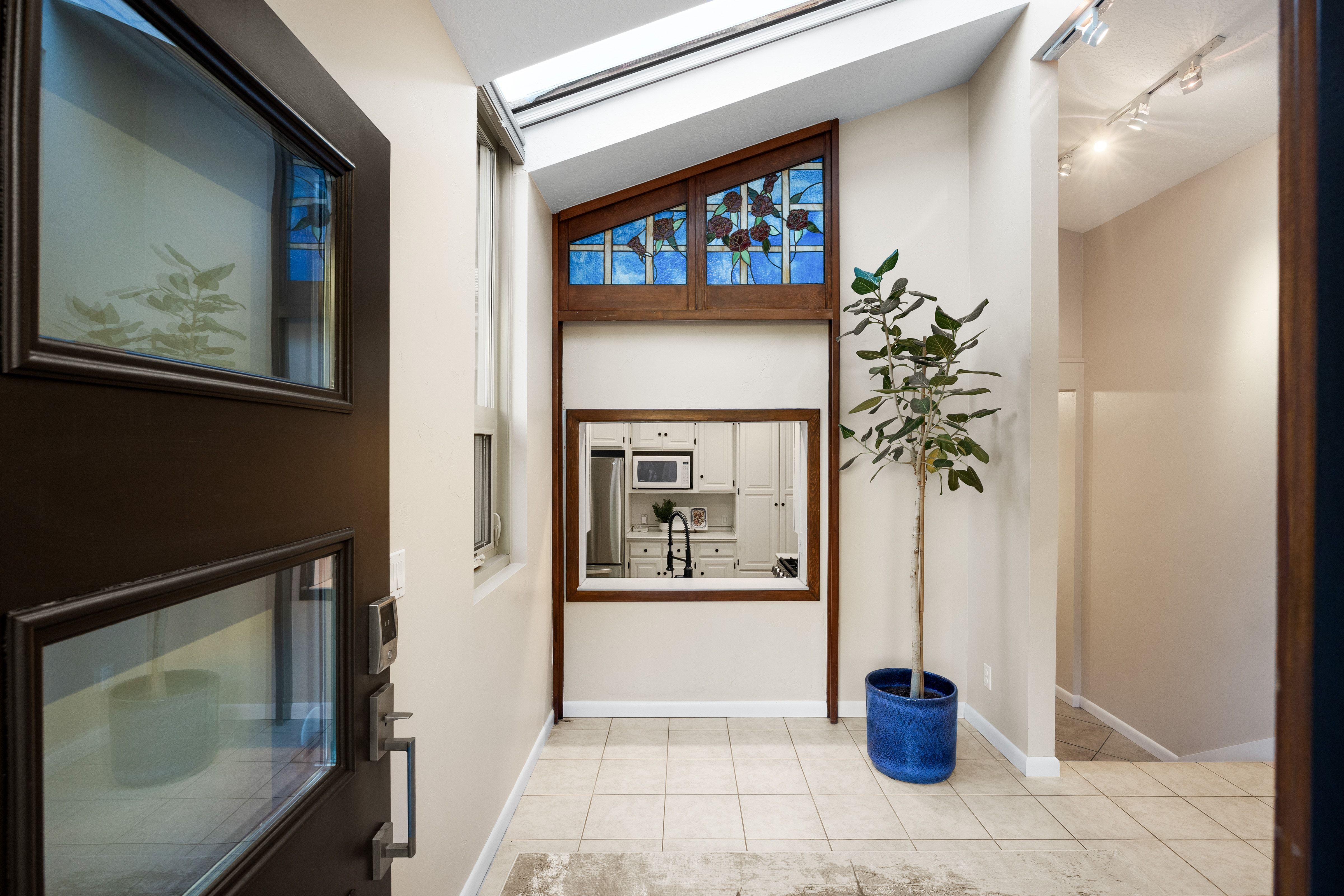 Foyer featuring tile flooring, a dark wood-framed window looking into the kitchen, a skylight, and a decorative stained glass window with wood trim