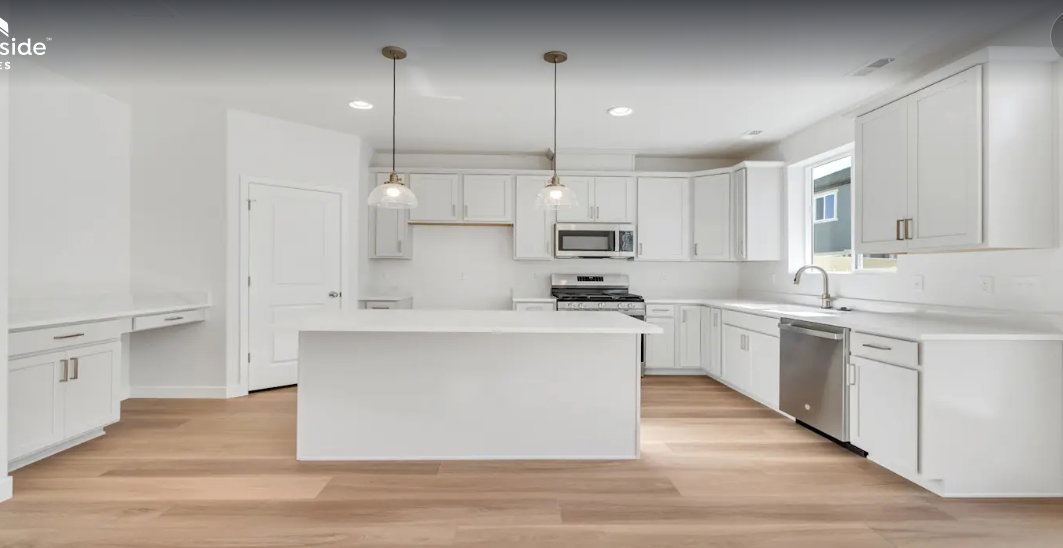 Modern kitchen featuring white shaker cabinetry, an expansive center island, integrated stainless steel appliances, wood-finish flooring, and pendant lighting