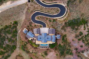 Spacious property featuring a serpentine driveway, extensive hardscaping, a multi-level home with a blue-tiled roof, and an exterior swimming pool