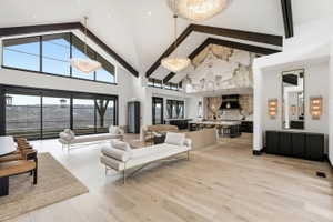 Expansive living area featuring vaulted ceilings with exposed beams, large format windows, wood-finish flooring, and multiple crystal chandeliers