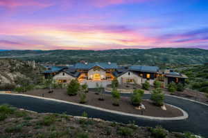 Expansive property featuring a stone and dark-paneled exterior, multiple gabled roofs, a paved circular driveway, and integrated outdoor lighting