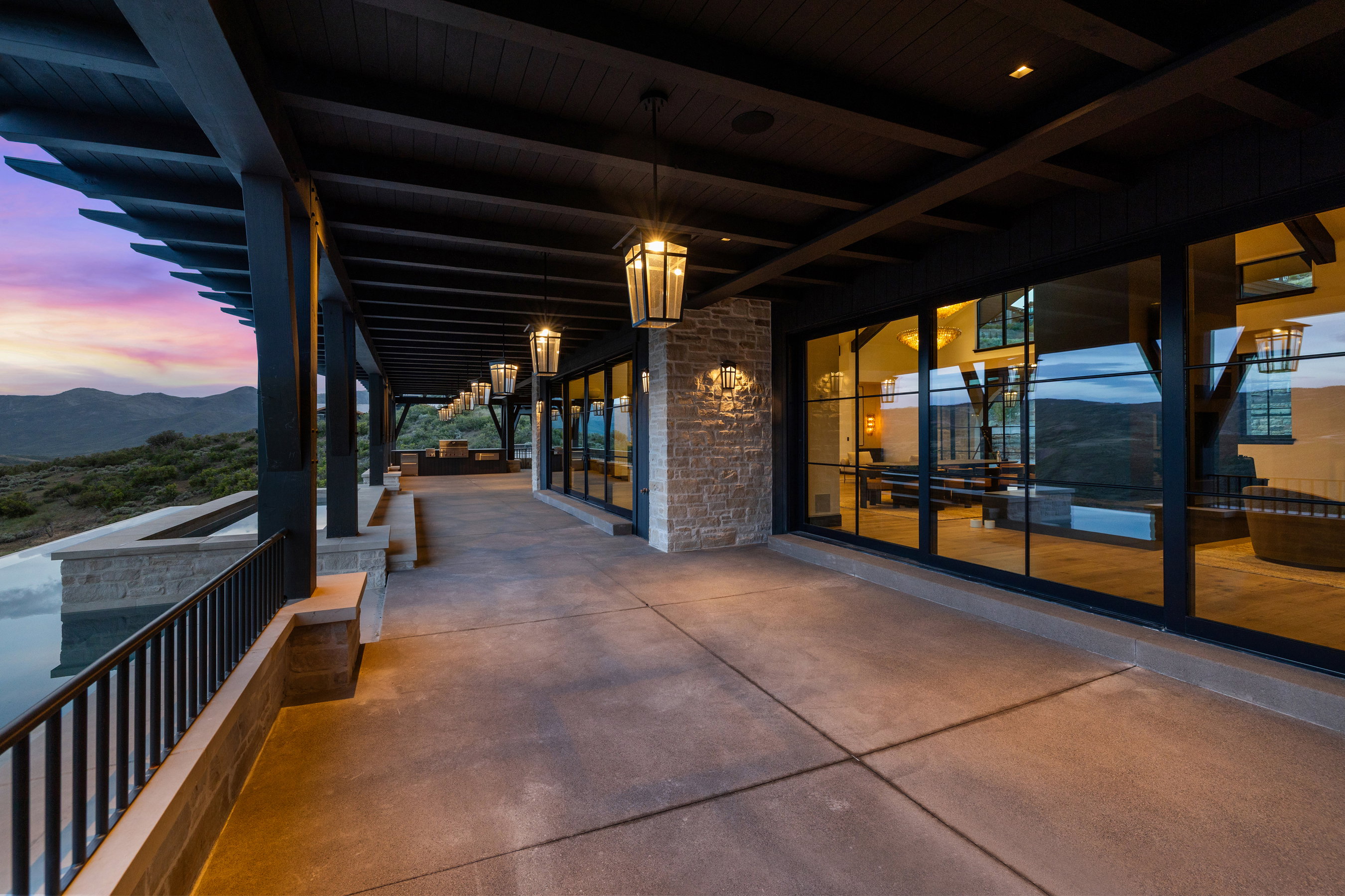 Expansive covered patio featuring a concrete surface, black beam pergola, and a stone wall accent