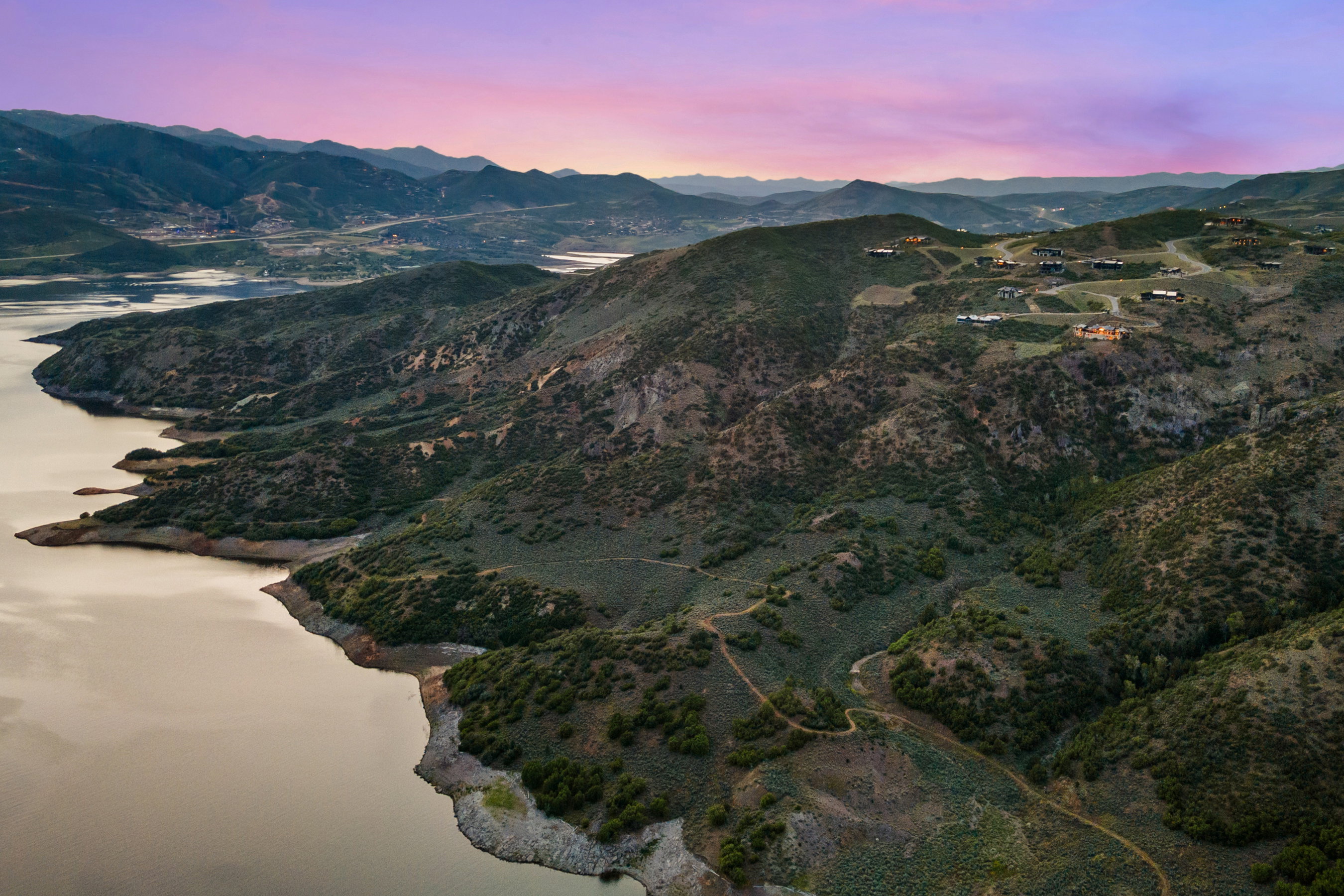Expansive mountain landscape featuring a large body of water, rolling hills, and scattered residential properties