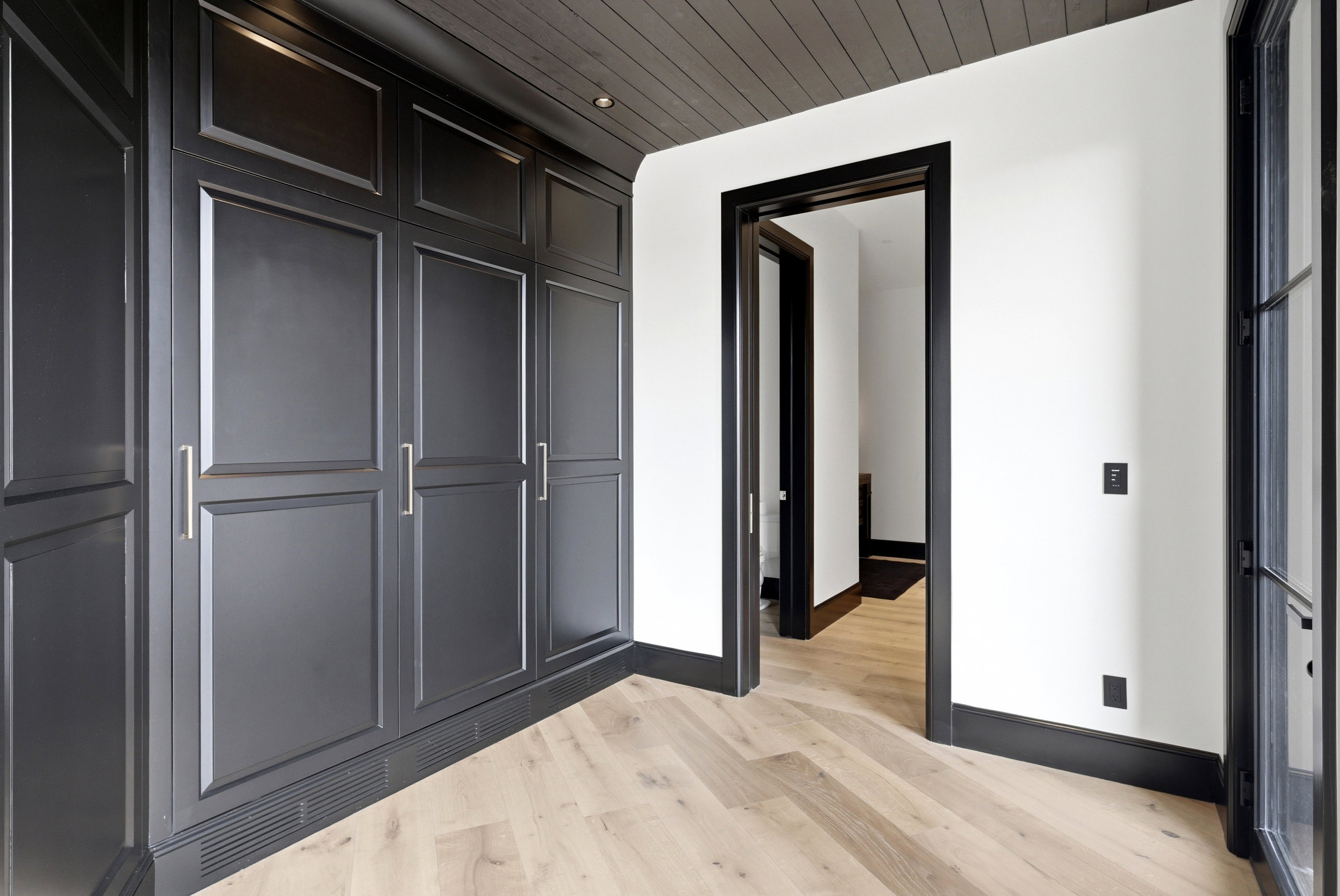 Built-in black panel cabinetry with brushed nickel hardware, herringbone wood-finish flooring, dark wood-paneled ceiling, dark trim, and recessed lighting