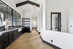 Expansive multi-paned windows illuminate a modern wet bar featuring a farmhouse sink, brass faucet, and dark custom cabinetry with stone countertops