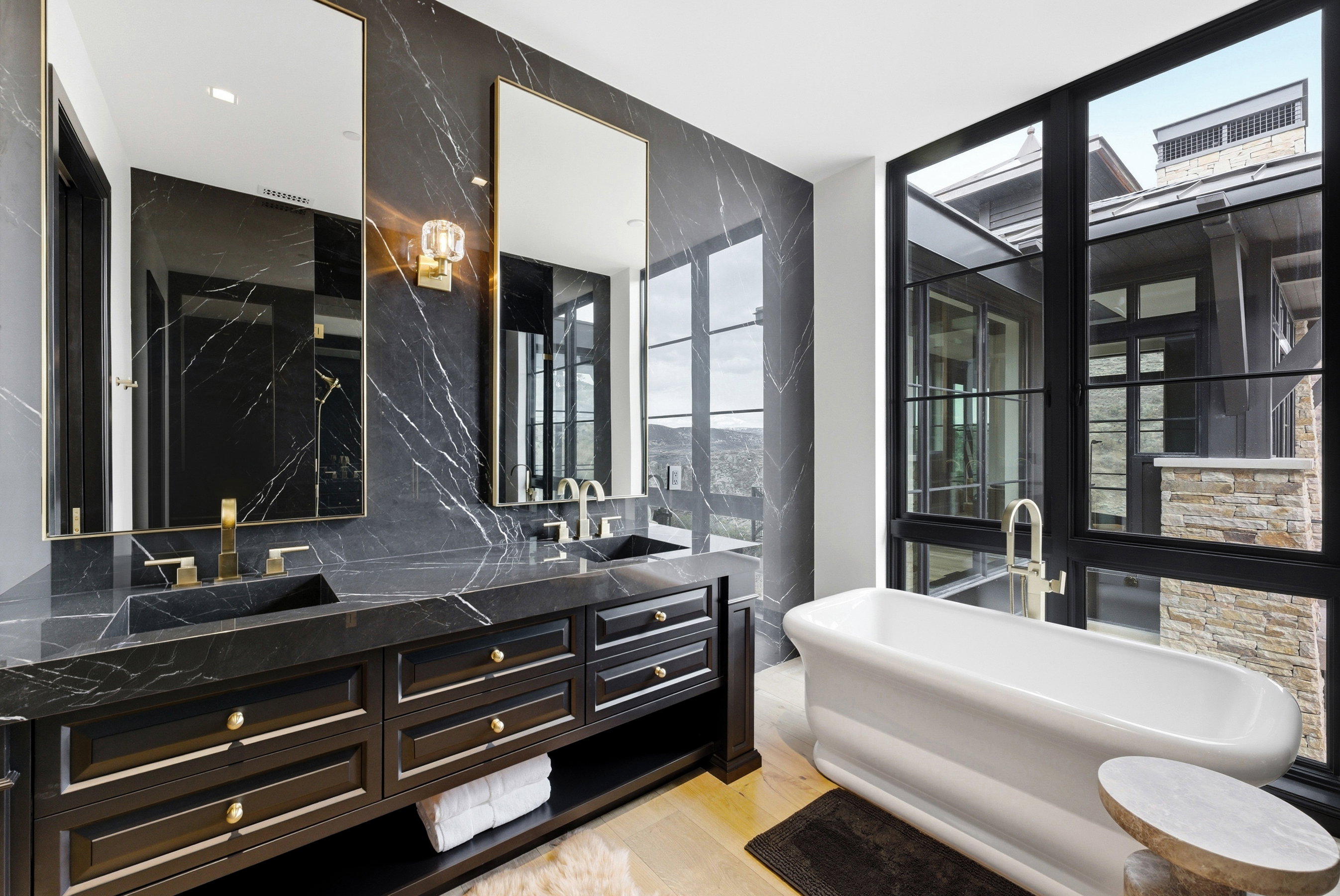 Luxurious bathroom featuring a freestanding soaking tub, expansive black-framed windows, and a dual vanity with integrated sinks