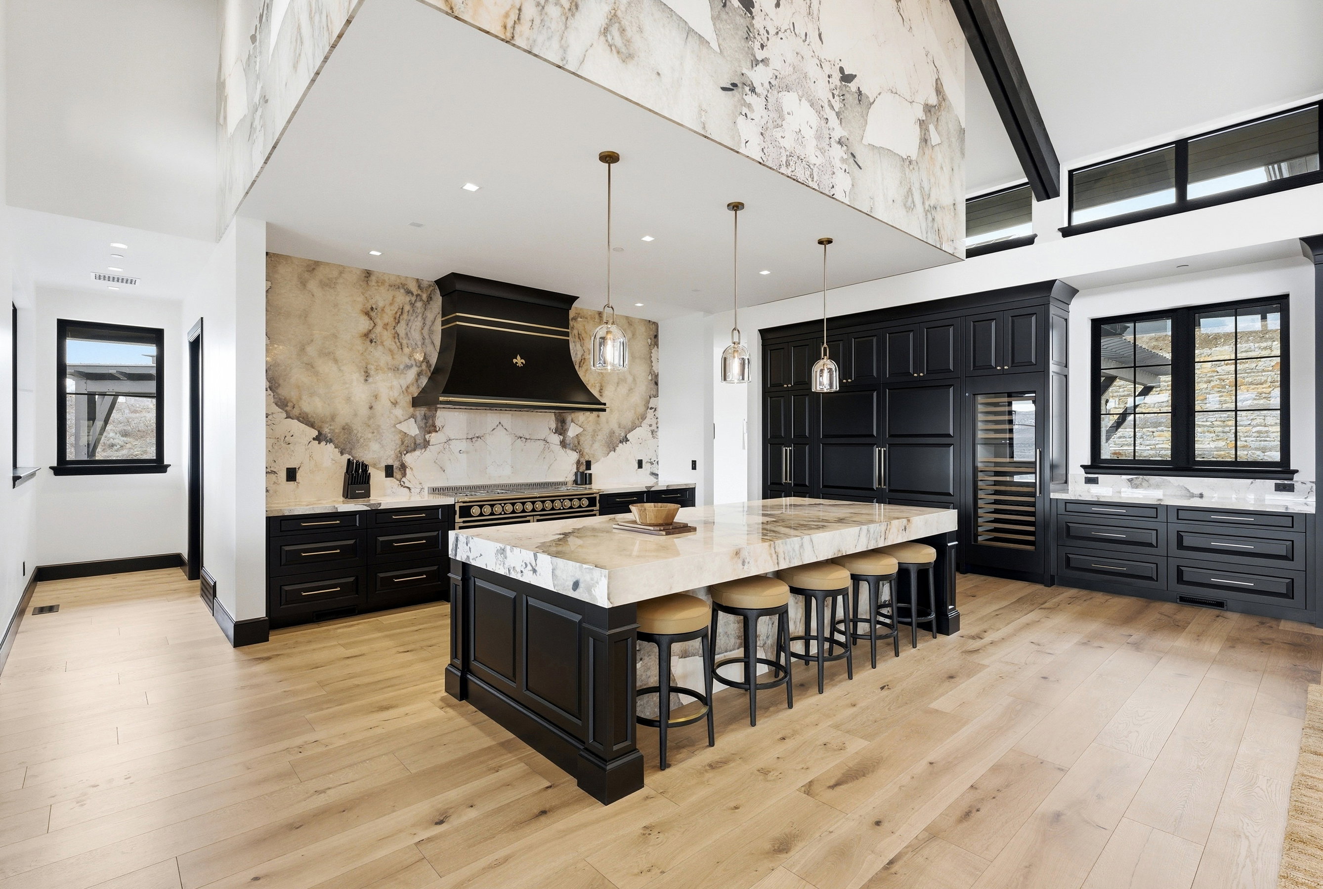 Expansive kitchen featuring a large central island with seating, dark wood cabinetry, a built-in wine cooler, and light wood-finish flooring