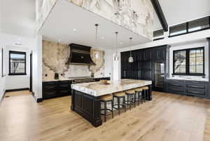 Expansive kitchen featuring a large central island with seating, dark wood cabinetry, a built-in wine cooler, and light wood-finish flooring
