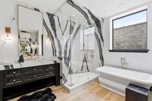 Bathroom featuring a freestanding tub, glass-enclosed shower, a double vanity with a stone countertop, and light wood-finish flooring