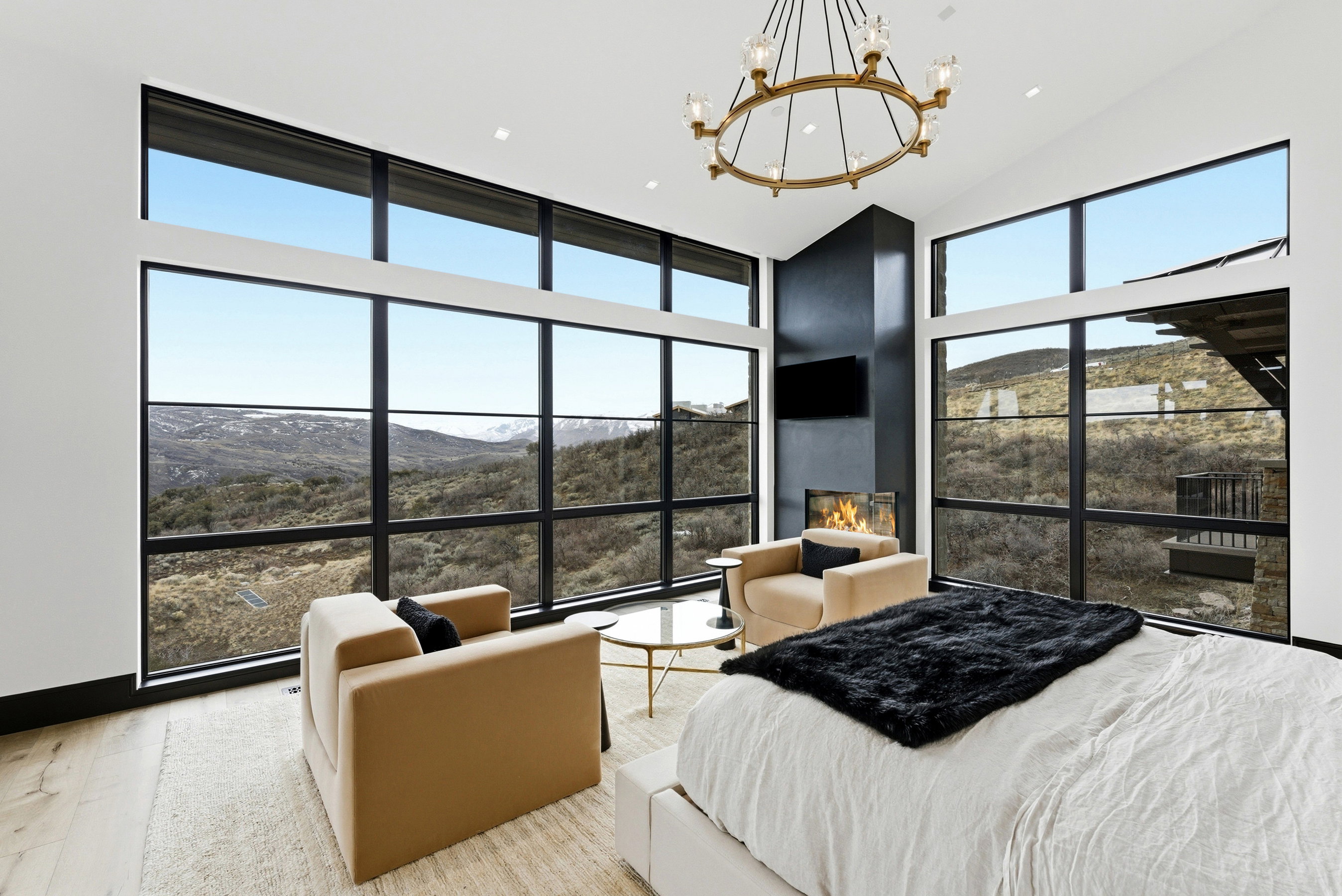 Room featuring expansive windows with black frames, a black fireplace surround, a built-in linear fireplace, wood-finish flooring, and a large chandelier with gold-tone accents