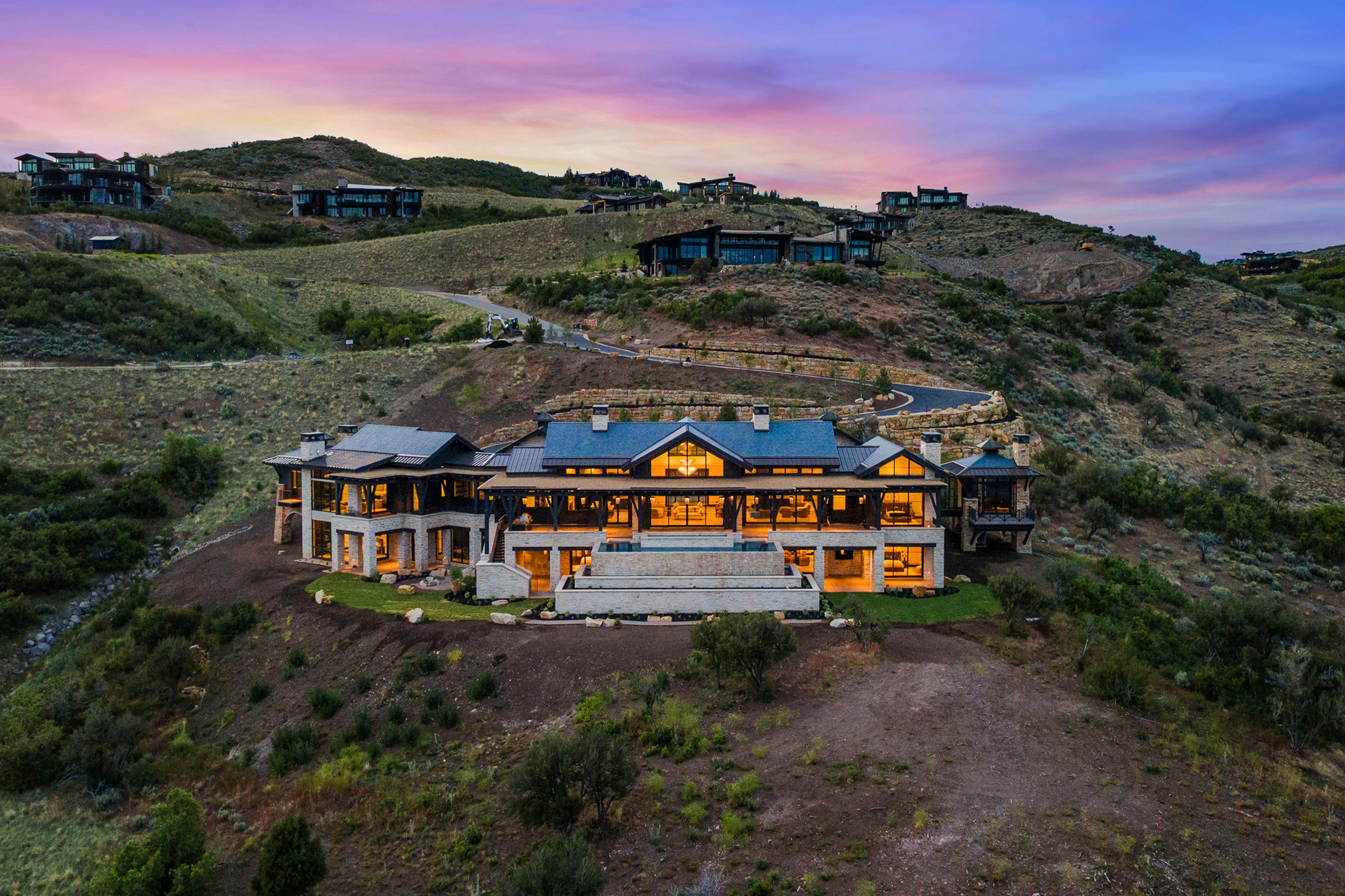 Expansive contemporary residence featuring a dark-toned roof, multiple large windows, and a prominent stone-clad exterior