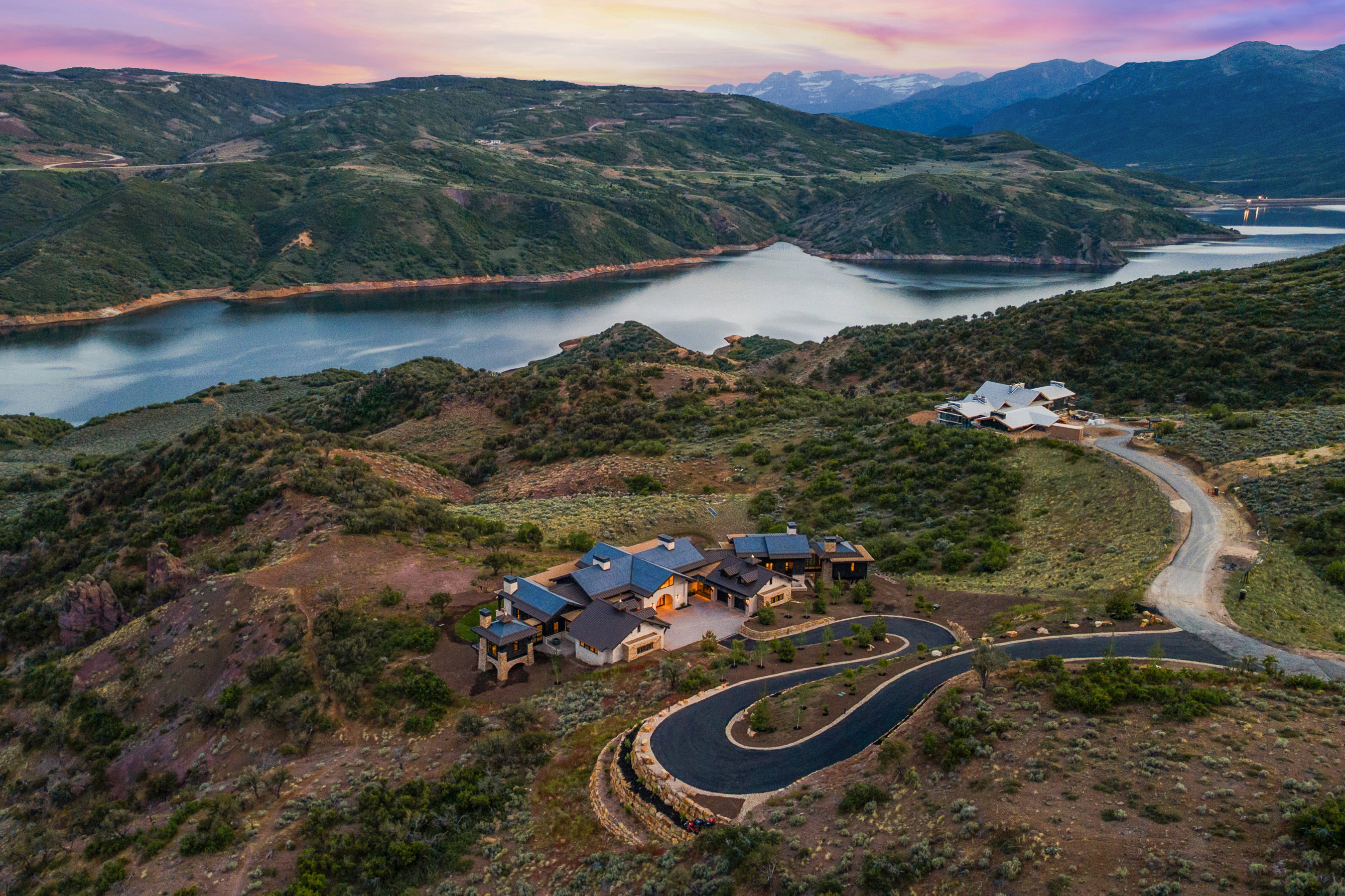 Hillside property featuring a winding paved driveway and a multi-level residence with a dark roof
