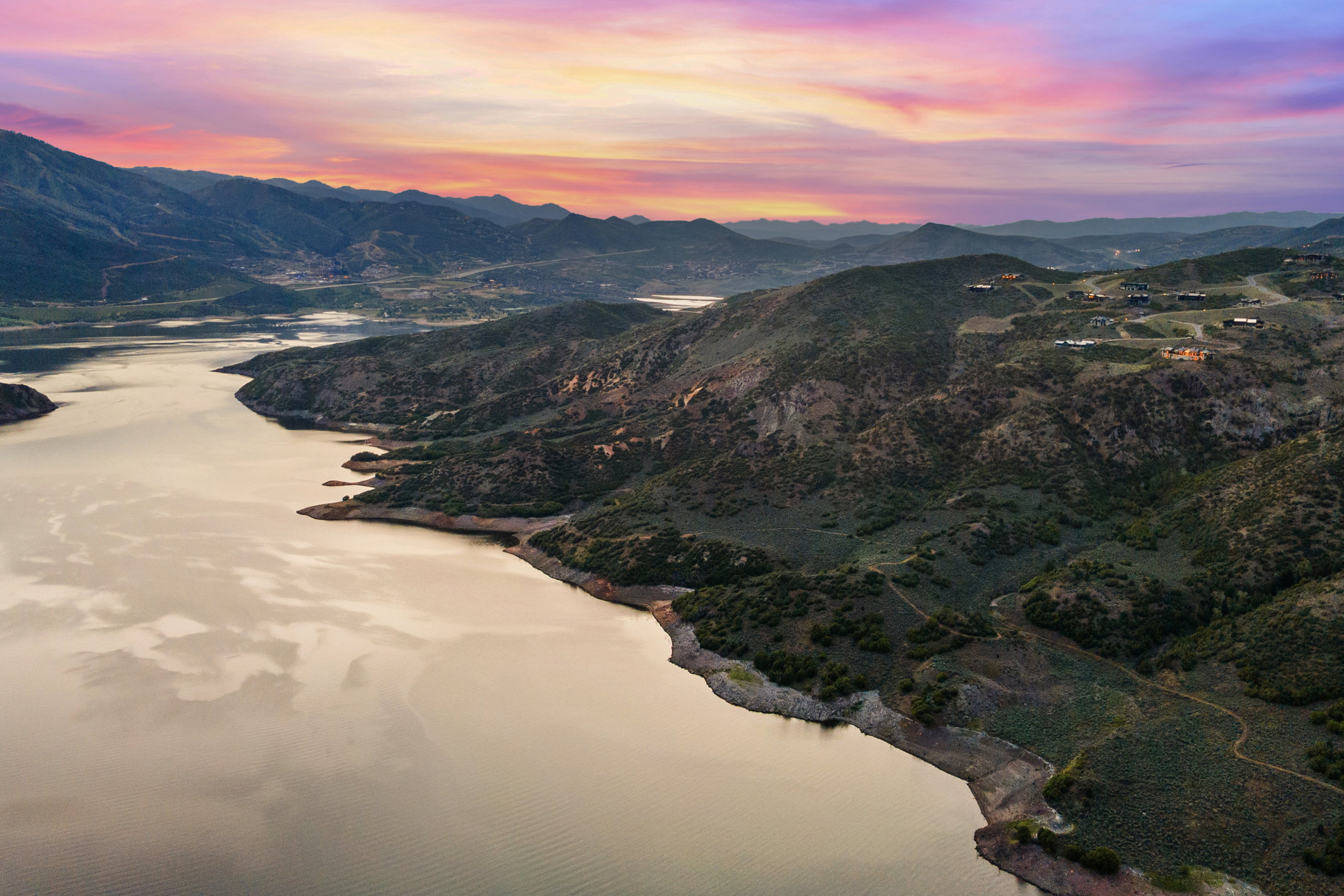 Expansive water body bordered by mountainous terrain, featuring scattered residences on the hillsides