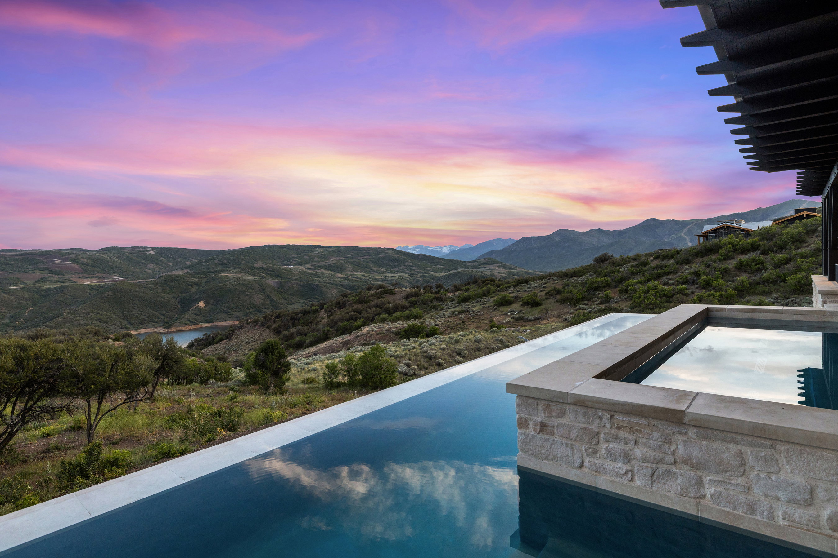 Infinity-edge pool with an integrated spa, featuring a natural stone facade and stone coping