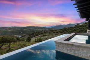 Infinity-edge pool with an integrated spa, featuring a natural stone facade and stone coping