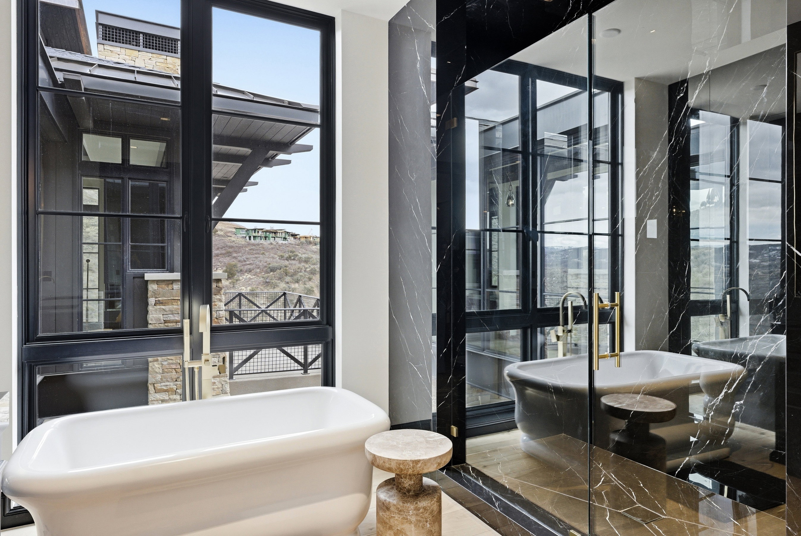 Freestanding soaking tub positioned before expansive black-framed windows