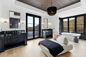 Spacious bathroom featuring light wood-finish flooring, a freestanding soaking tub, and dual vanity areas with black cabinetry and countertops