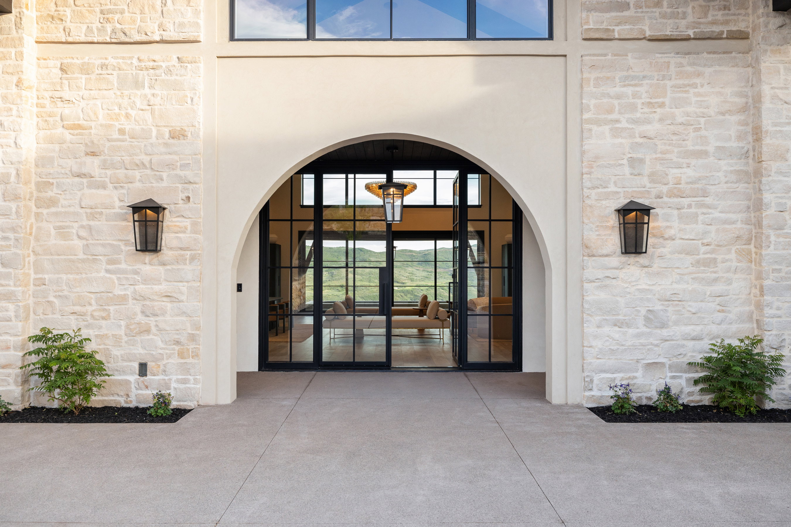 Stone facade entrance featuring a grand arched doorway, black-framed glass double doors, transom windows, and exterior wall lanterns