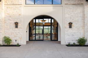 Stone facade entrance featuring a grand arched doorway, black-framed glass double doors, transom windows, and exterior wall lanterns