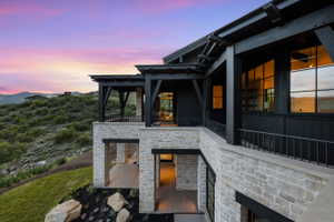 Multi-level exterior featuring natural stone veneer, black wood siding, extensive grid-pattern windows, and covered patios with metal railings