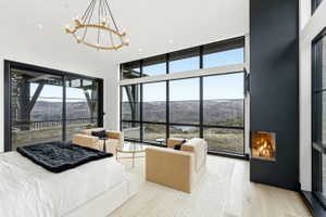 Spacious room featuring floor-to-ceiling windows, a built-in fireplace, a large sliding glass door, light wood-finish flooring, and a contemporary chandelier