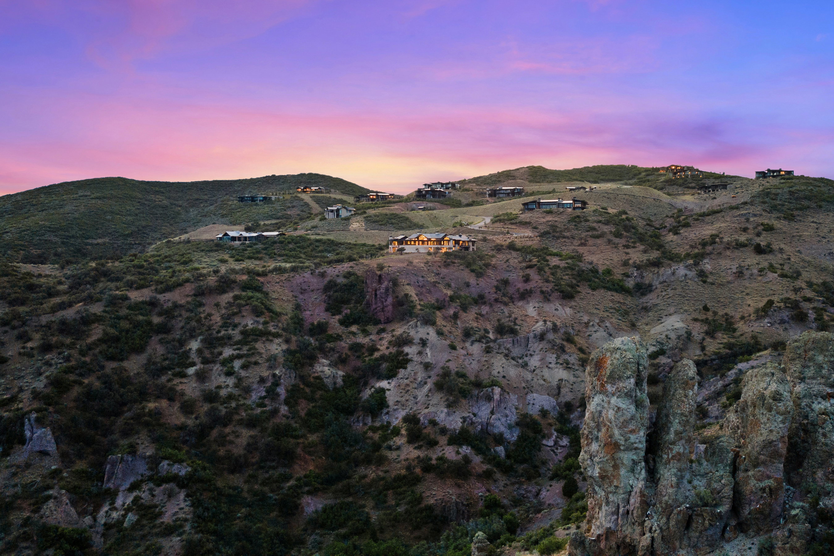 Mountainous terrain featuring dramatic rock formations and diverse vegetation under a colorful sky