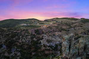 Mountainous terrain featuring dramatic rock formations and diverse vegetation under a colorful sky