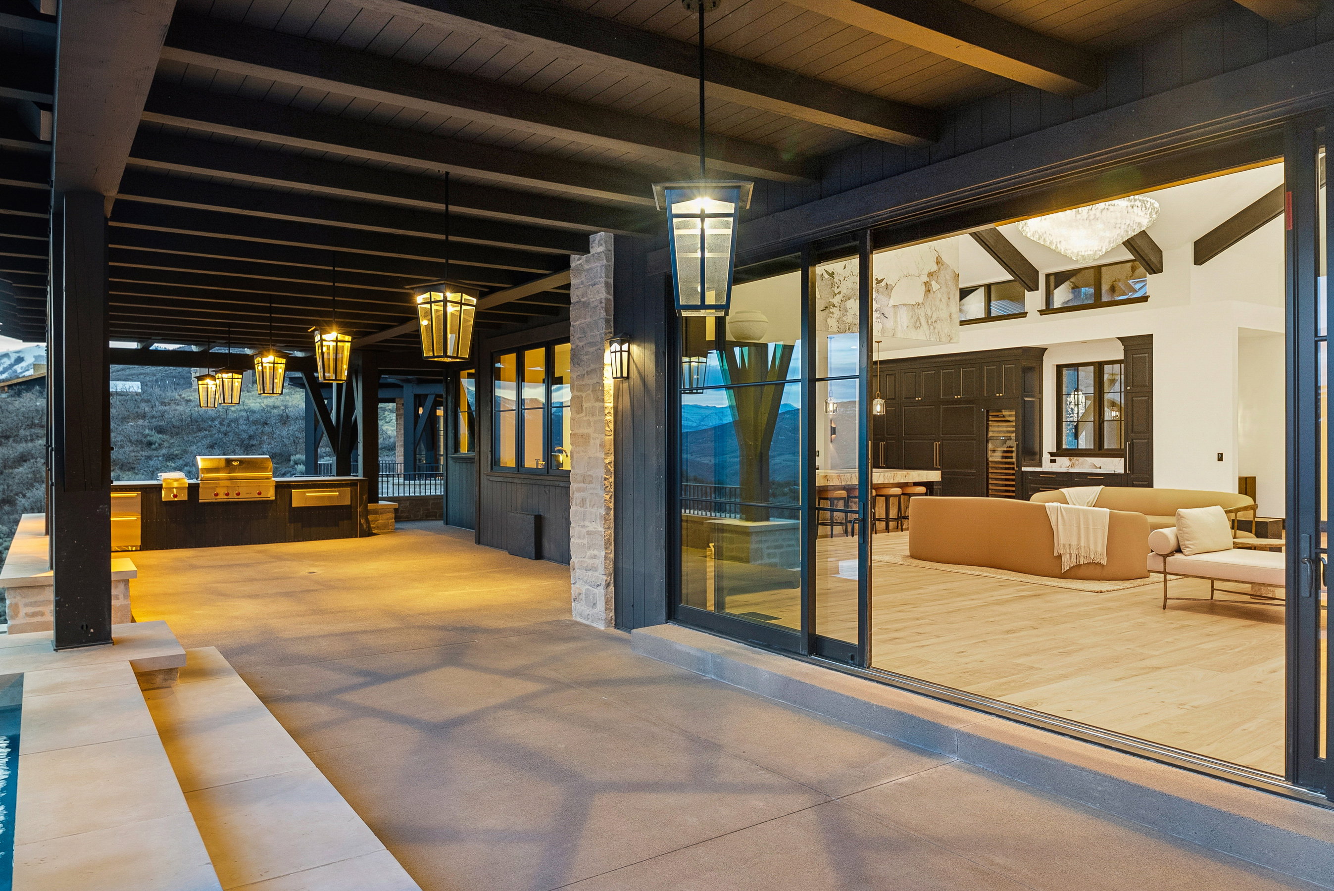 Expansive outdoor patio with a built-in grill station, concrete flooring, and a dark wood-beamed ceiling