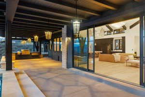 Expansive outdoor patio with a built-in grill station, concrete flooring, and a dark wood-beamed ceiling