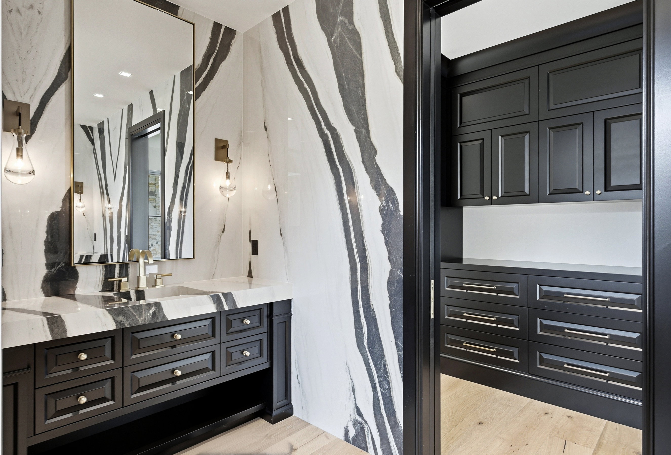 Bathroom featuring floor-to-ceiling veined stone walls, a large rectangular mirror, and an integrated stone sink