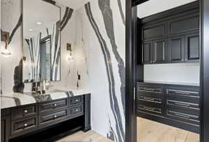 Bathroom featuring floor-to-ceiling veined stone walls, a large rectangular mirror, and an integrated stone sink