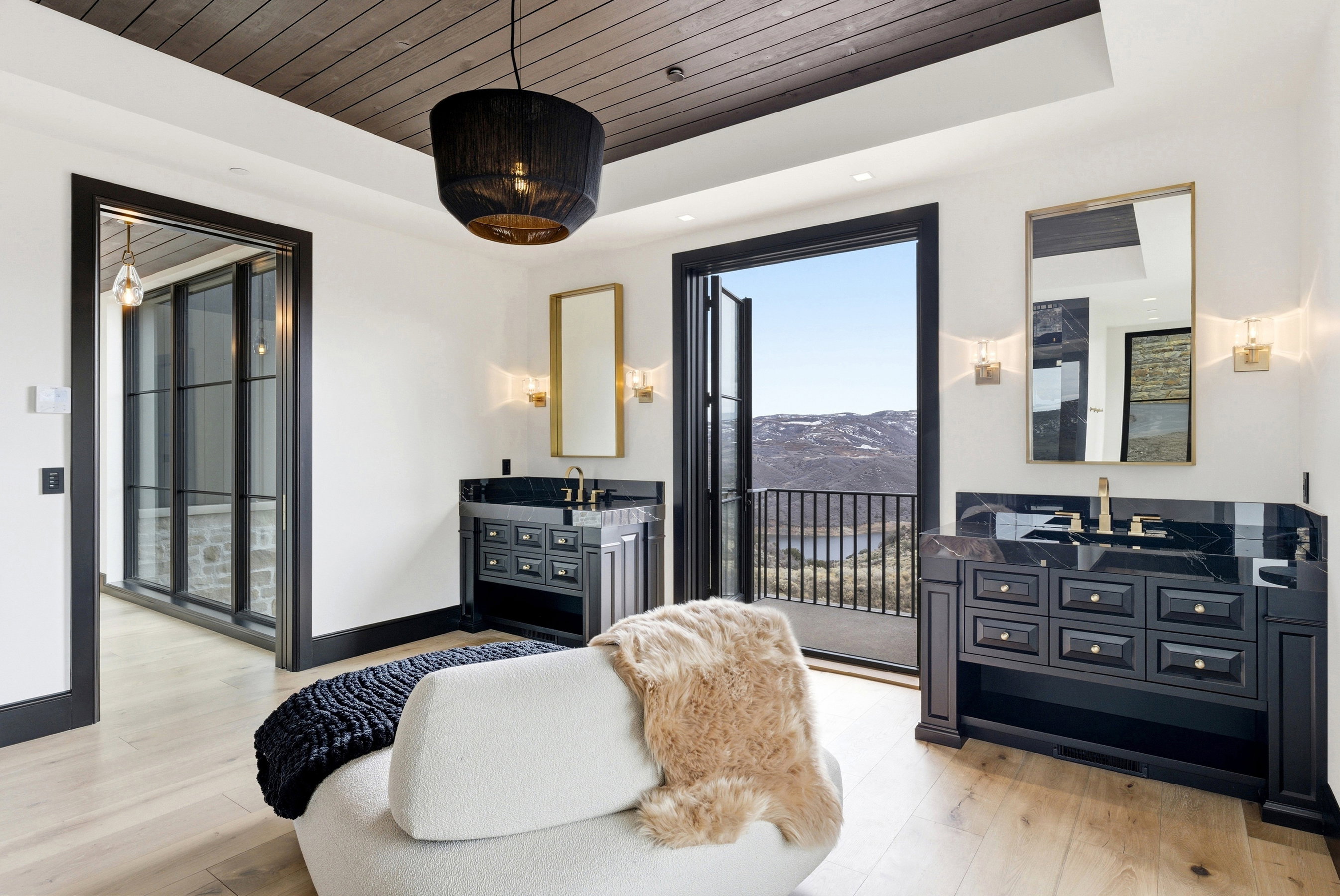 Bathroom featuring dual black vanities with dark countertops, a balcony with metal railing, wood-finish flooring, a wood-paneled ceiling, and a black drum-shade pendant light