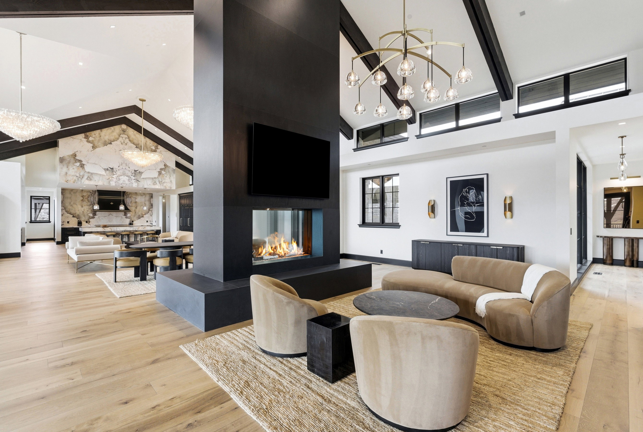 Expansive open-concept living space featuring high vaulted ceilings with exposed beams, wood-finish flooring, and a central fireplace with a built-in television